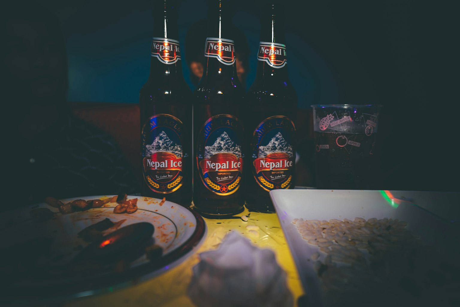 Three beer bottles on a table with a plate of food