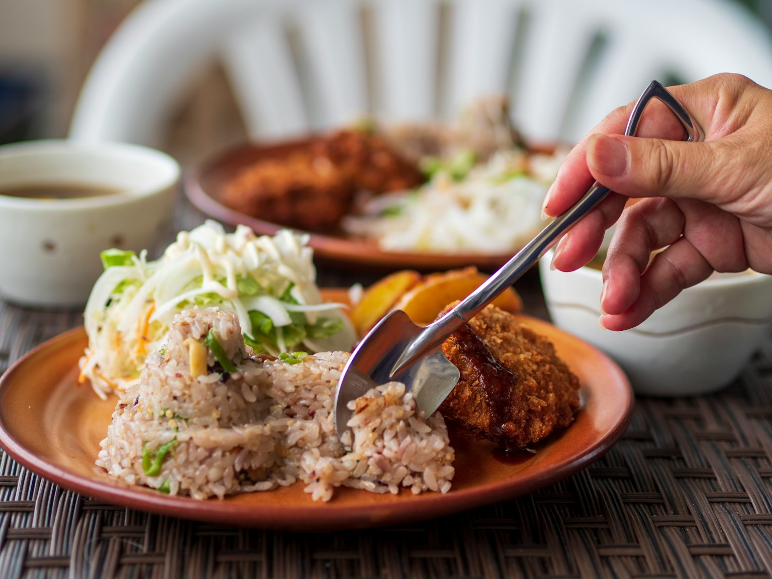 A plate of rice and salad with a hand cutting into the food using a fork