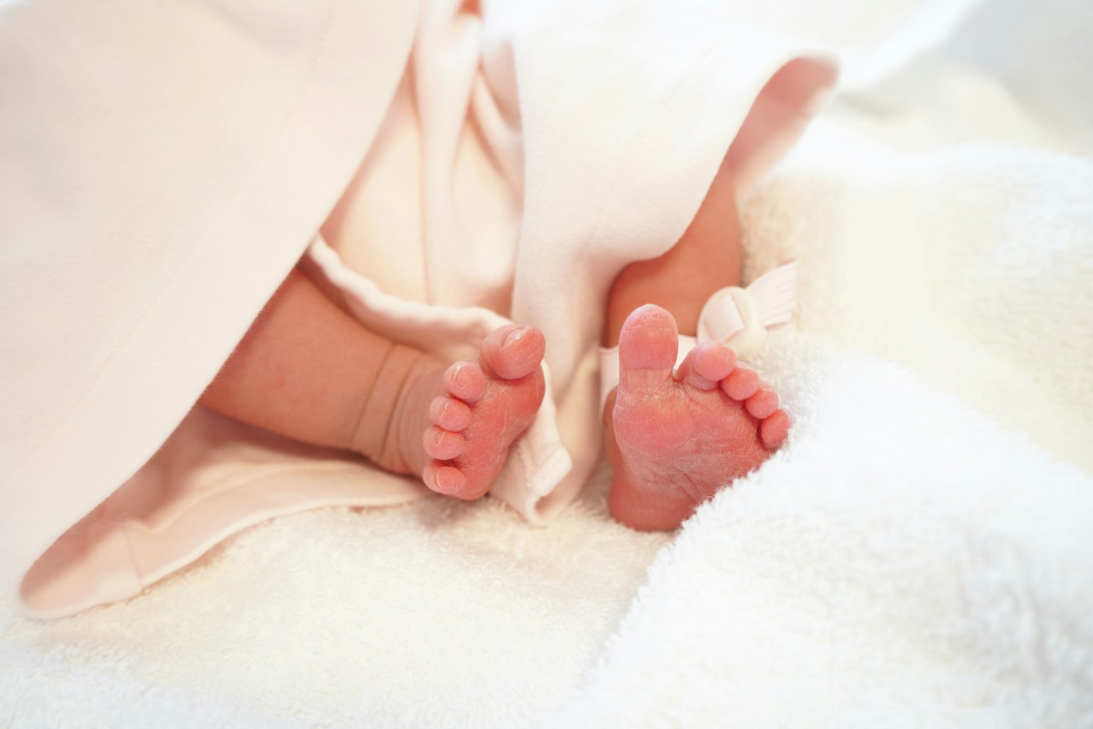 Kaki bayi kecil yang muncul dari selimut putih yang lembut