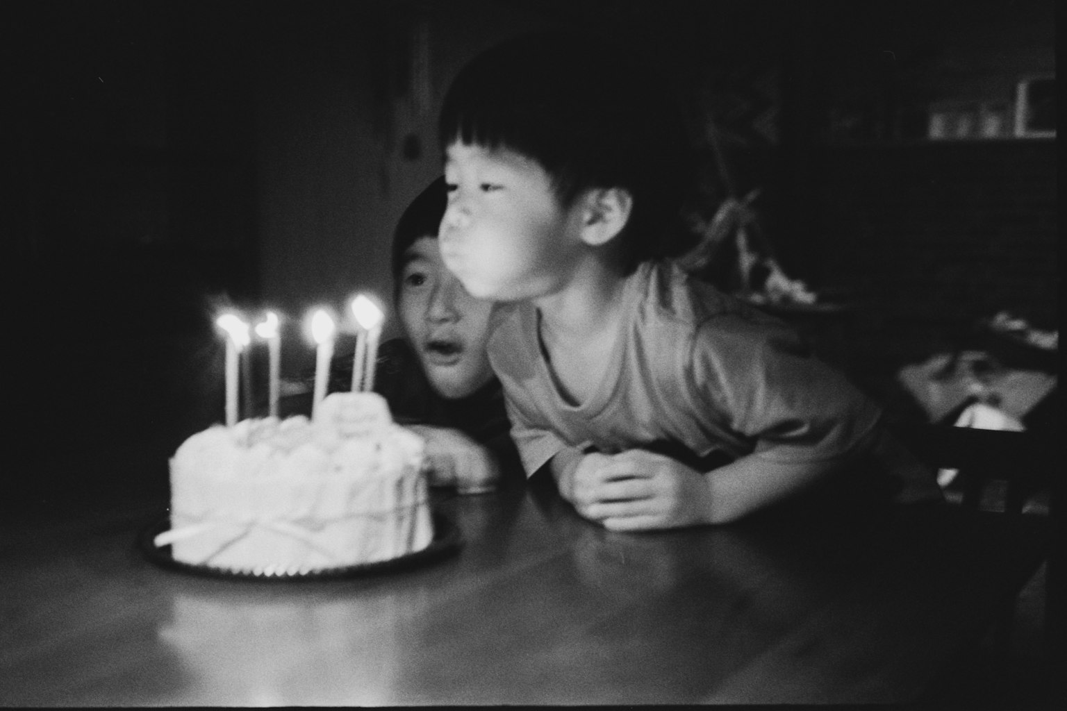 子供が誕生日ケーキのろうそくを吹き消そうとしているモノクロの写真