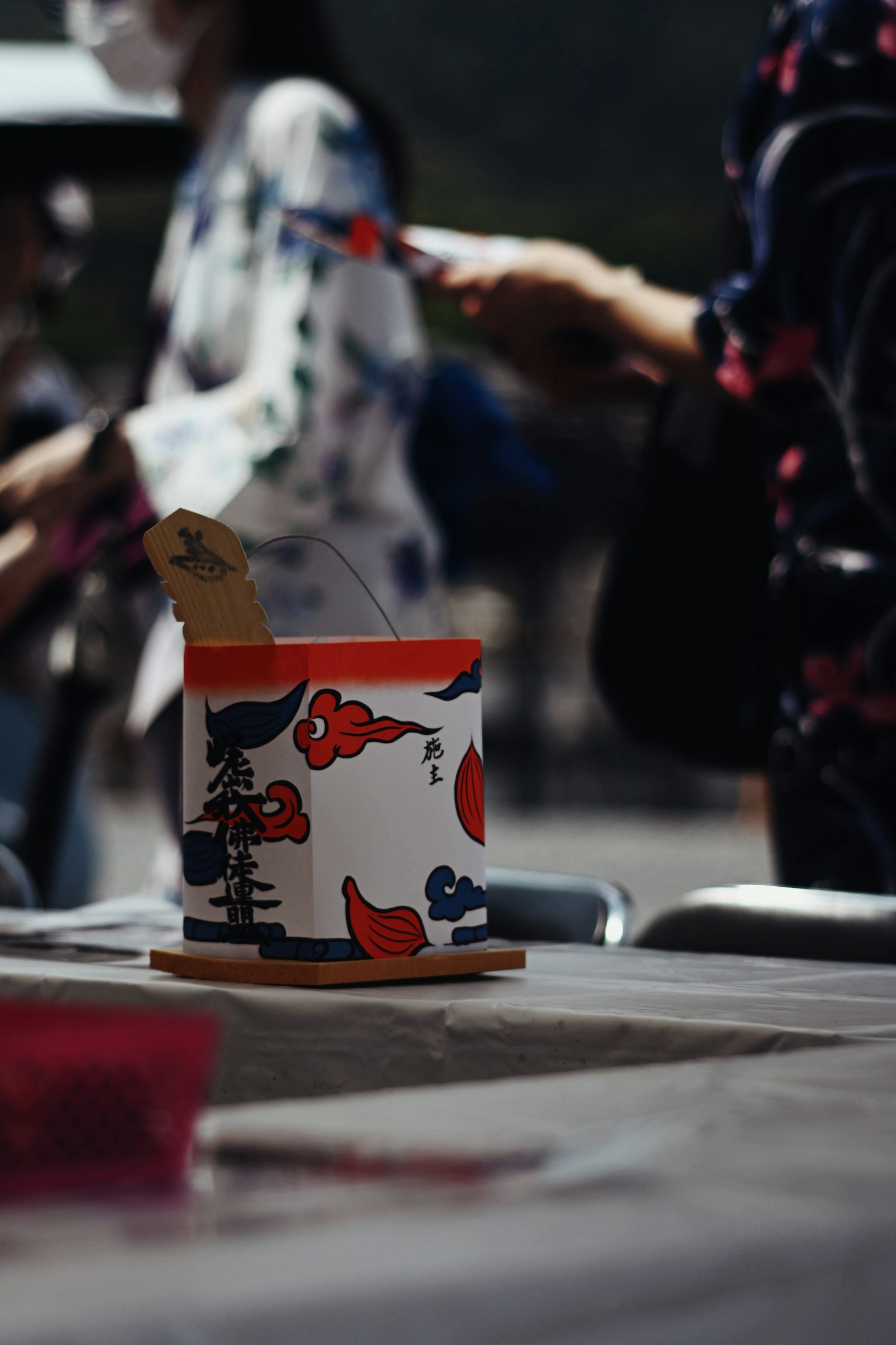 Un recipiente decorativo de estilo japonés con patrones coloridos colocado sobre una mesa rodeado de personas