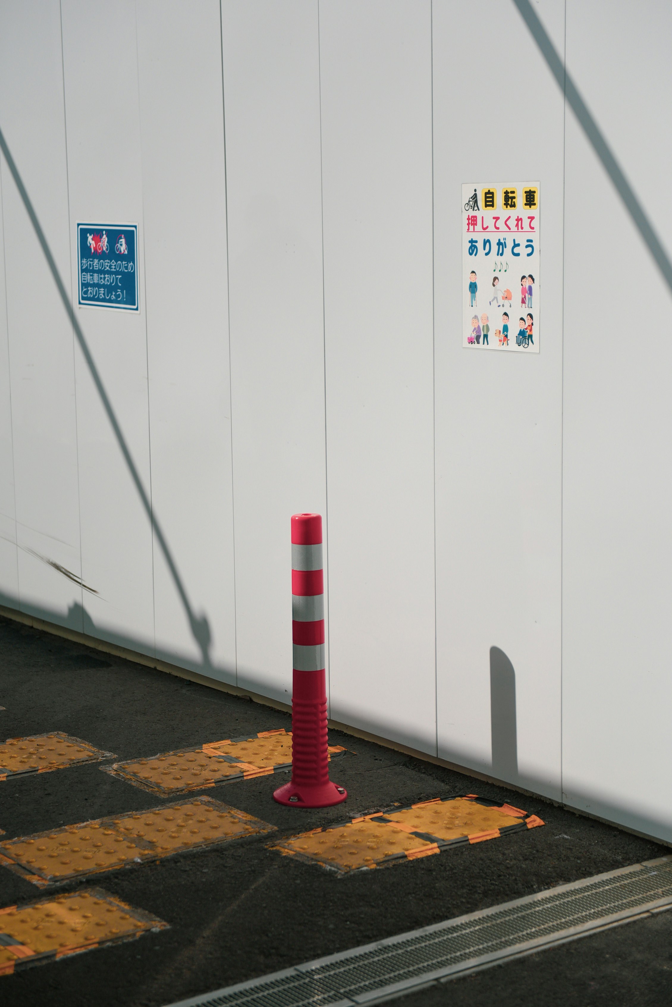 白い壁沿いの赤白のポールと黄色い点字ブロック