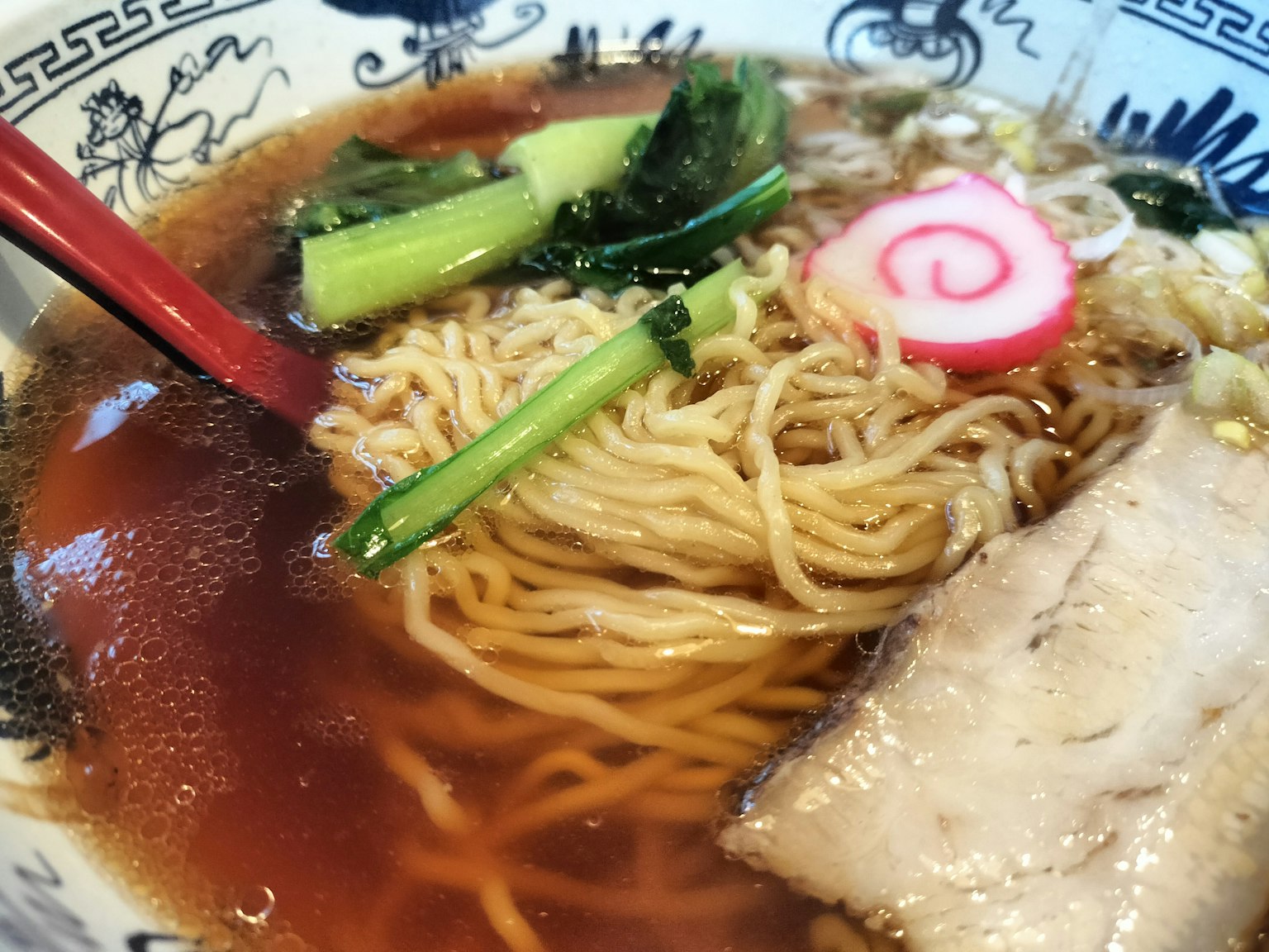 一碗美味的拉麵，配有湯、叉燒片、蔥、漩渦魚板和綠葉蔬菜