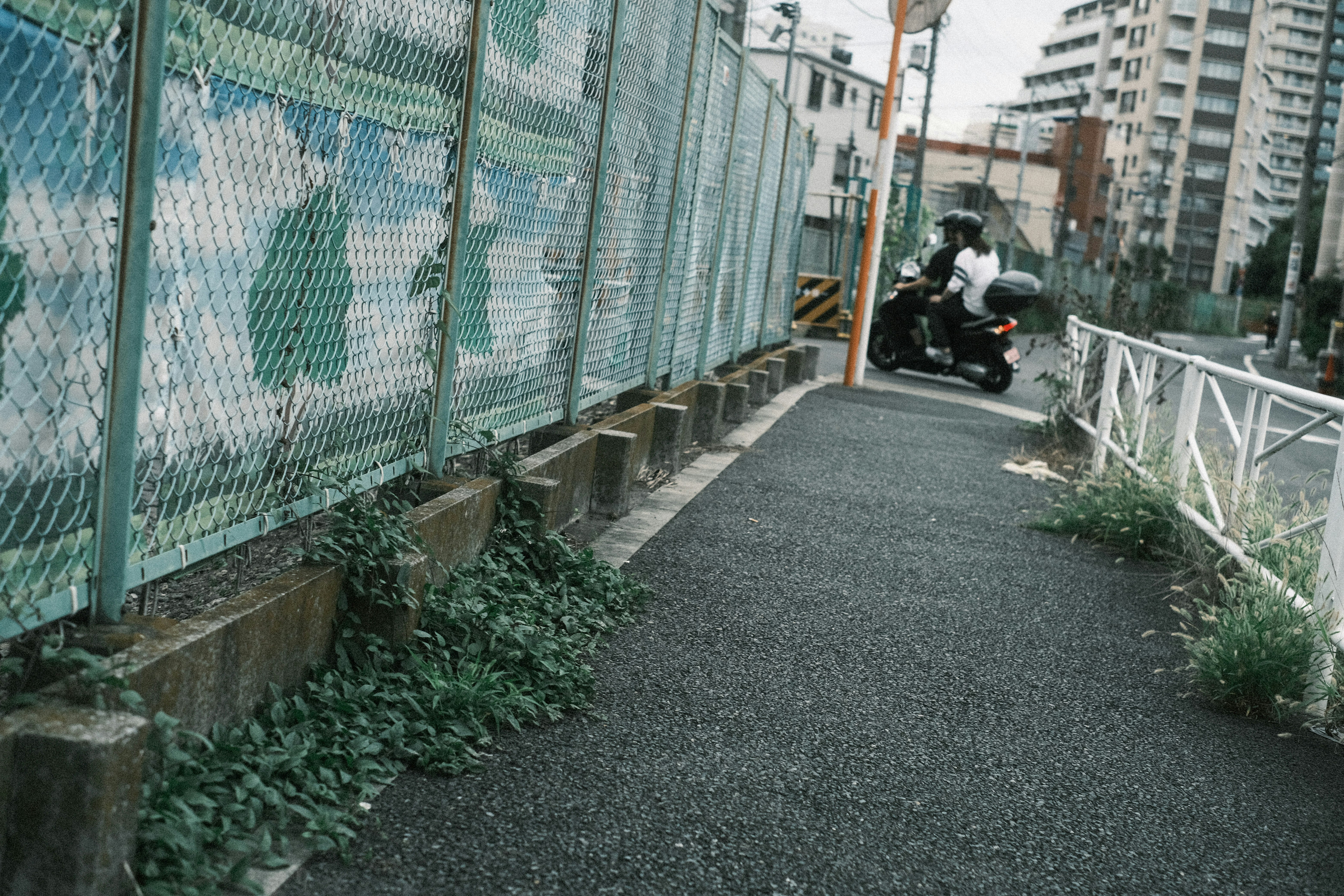 フェンス沿いの狭い路地を走るバイクと自転車のある風景