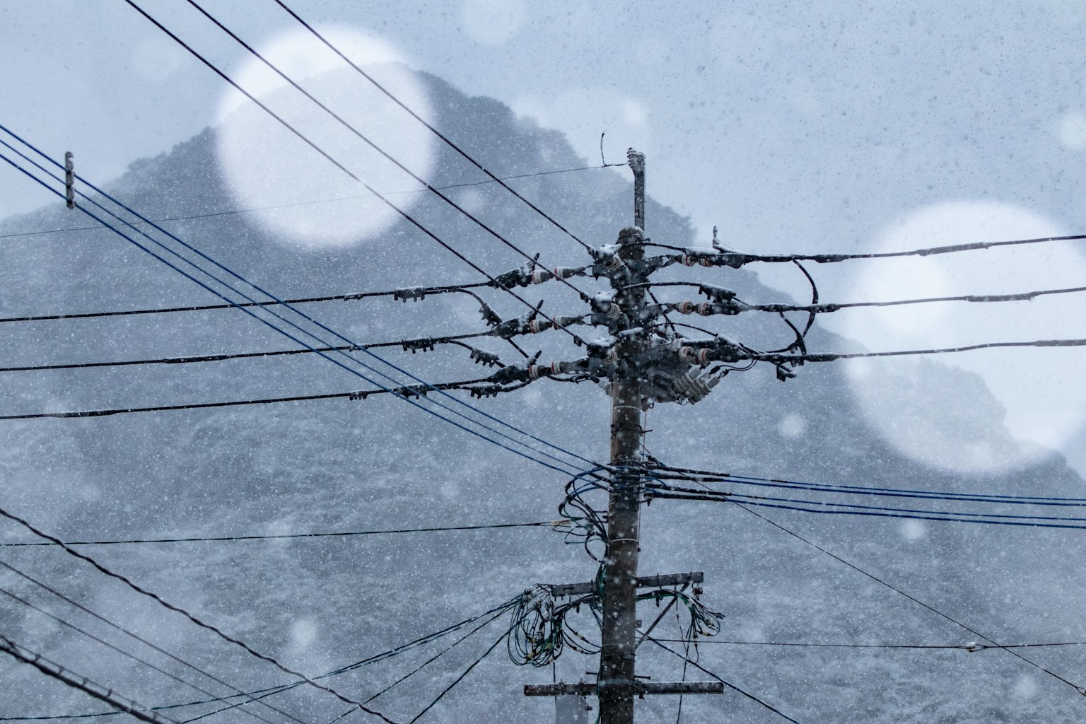 Utility pole and power lines with a snowy mountain background