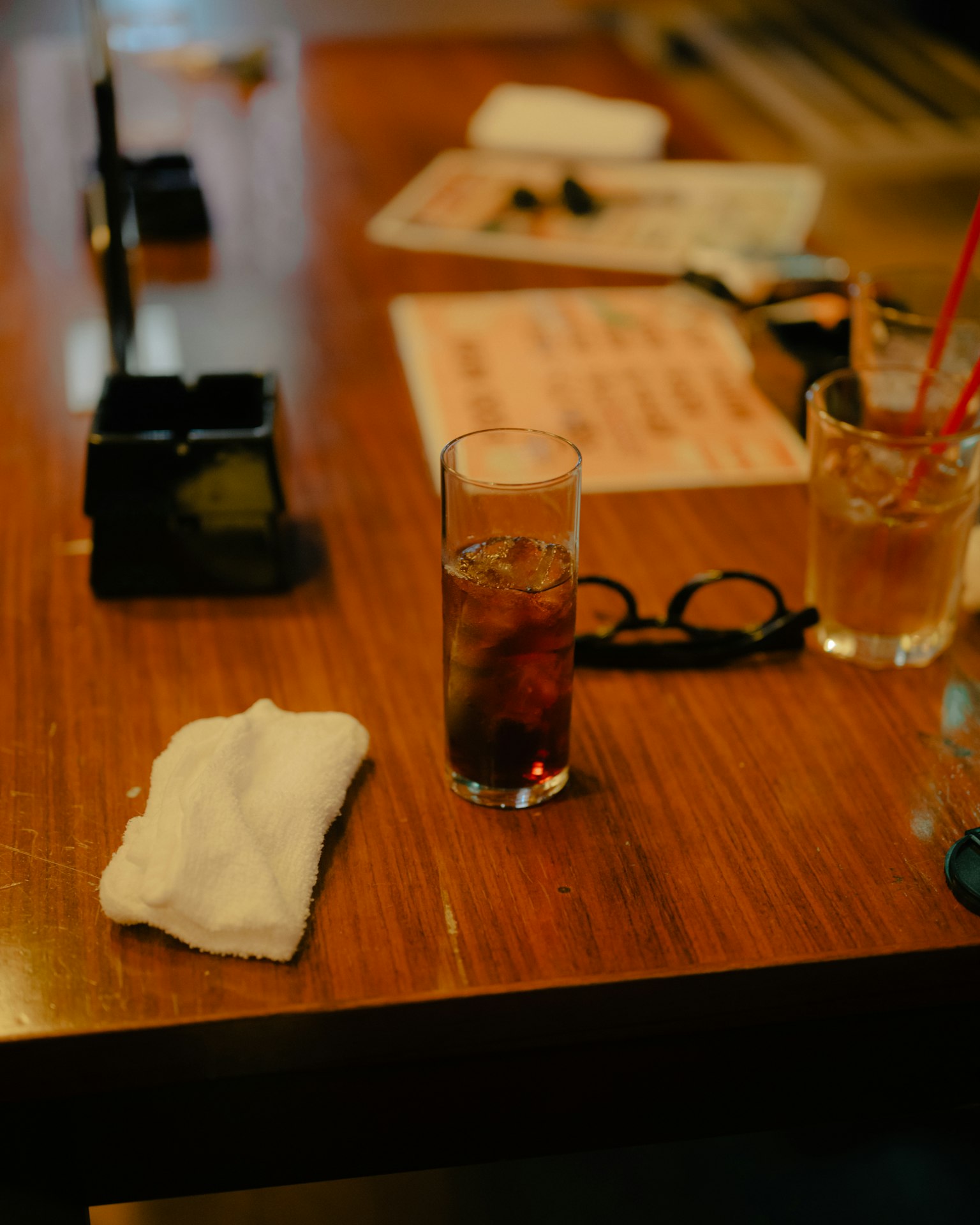 Un verre de boisson sur une table en bois avec une serviette et des lunettes à proximité