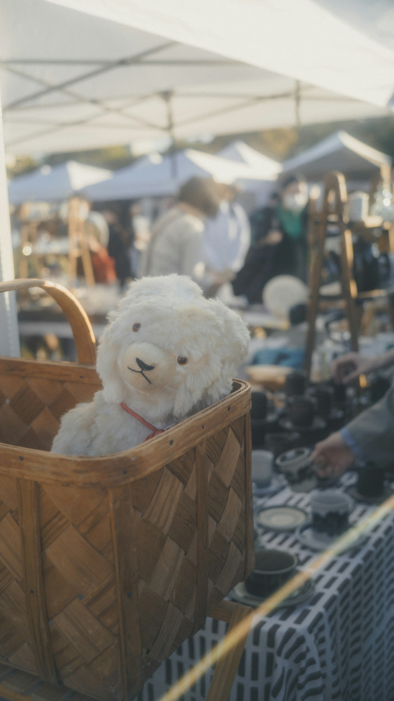 市場のバスケットに入った白いぬいぐるみのクマと背景の人々