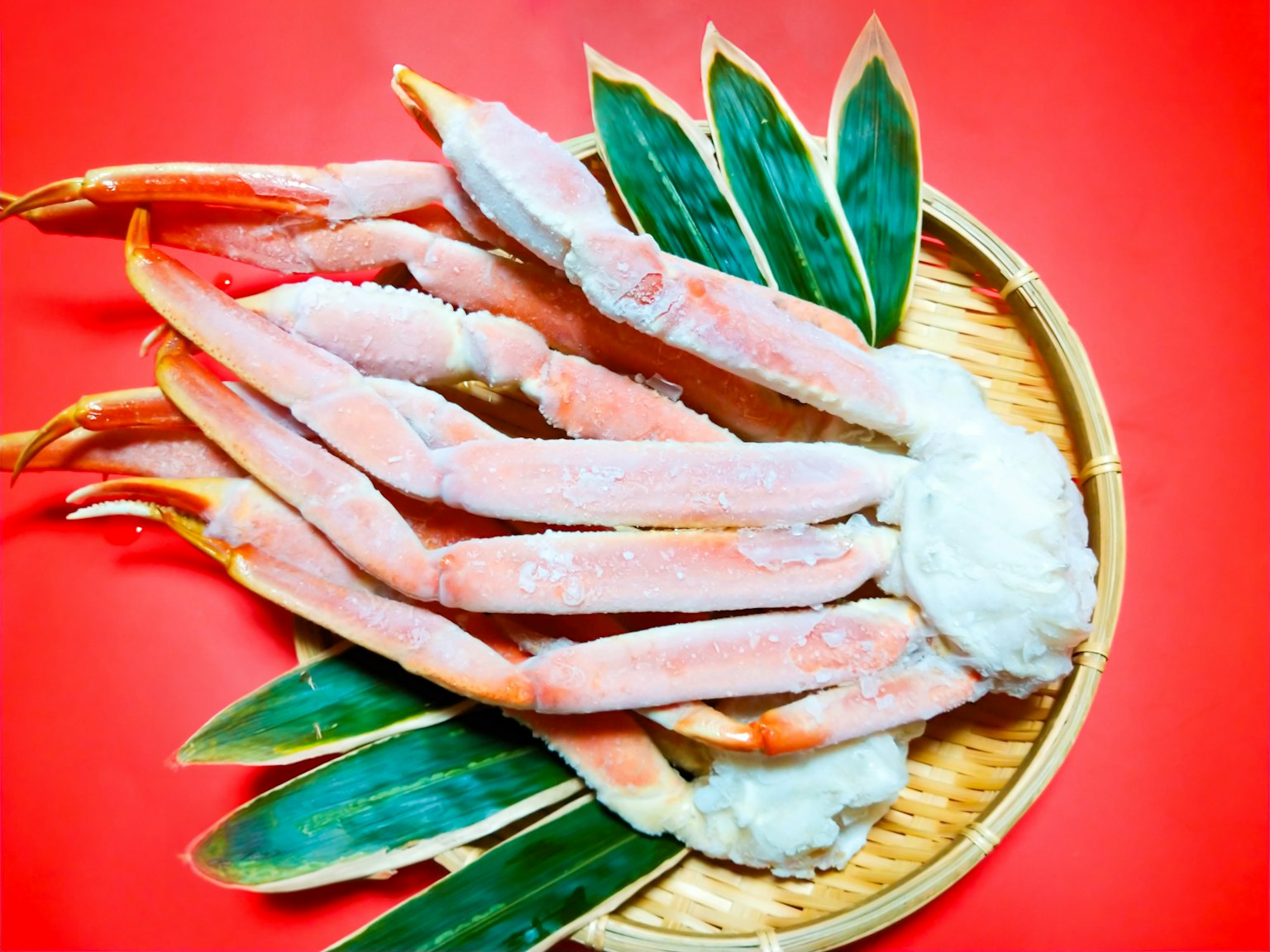 Crab legs arranged on a bamboo plate with green leaves on a red background