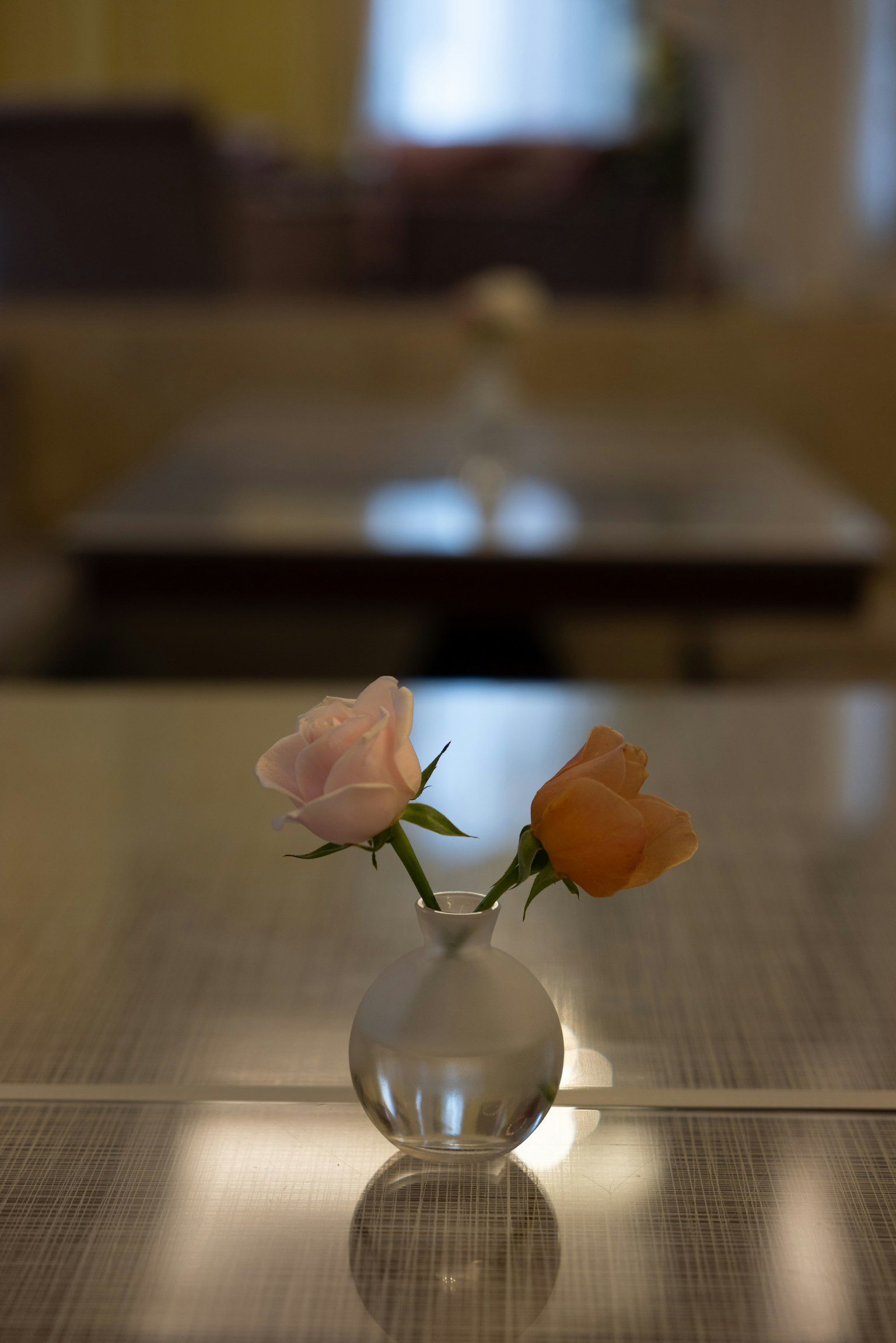 テーブルの上に置かれた小さなガラスの花瓶に入ったピンクとオレンジのバラの花