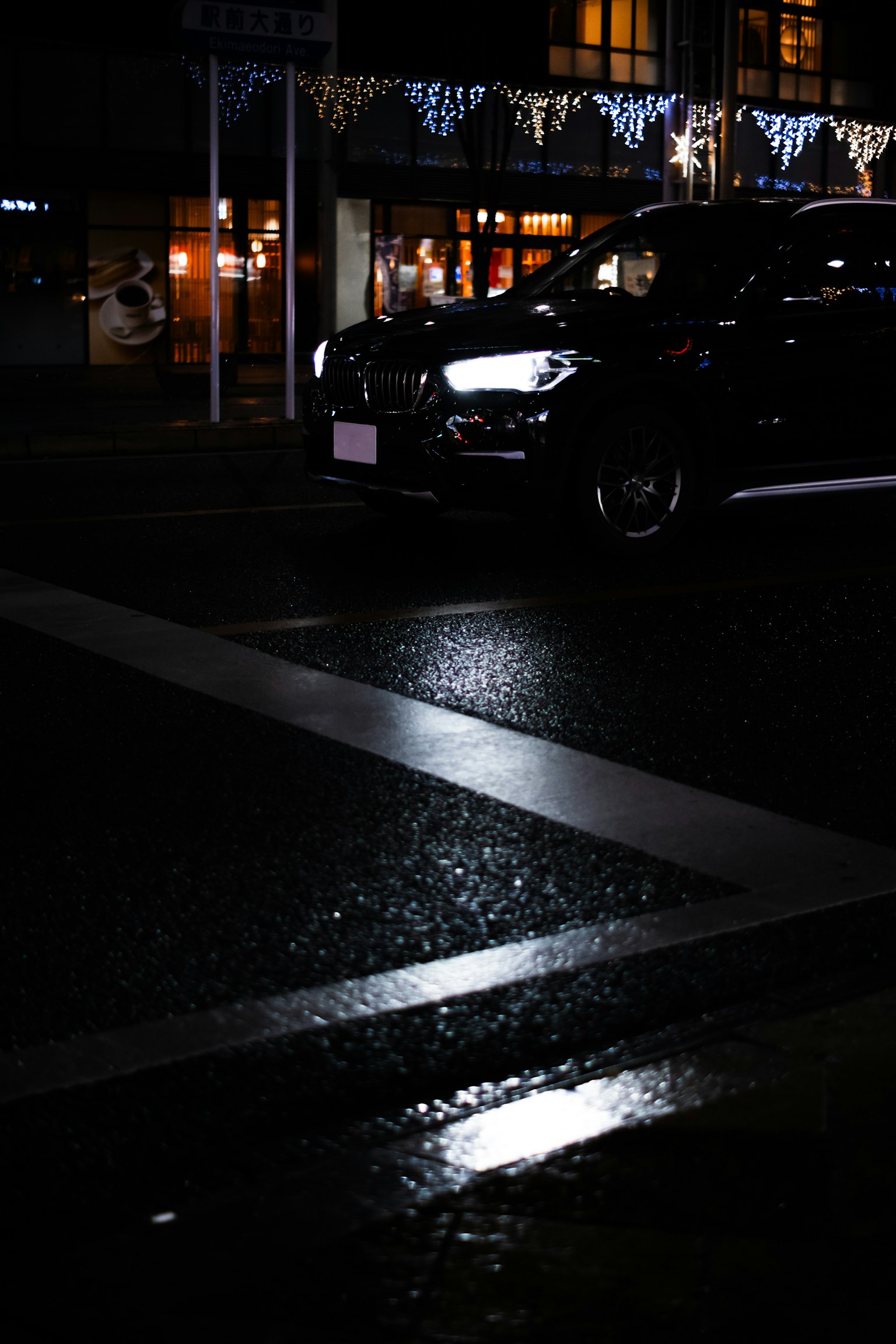 Auto nera a un incrocio bagnato con riflessi sulla strada