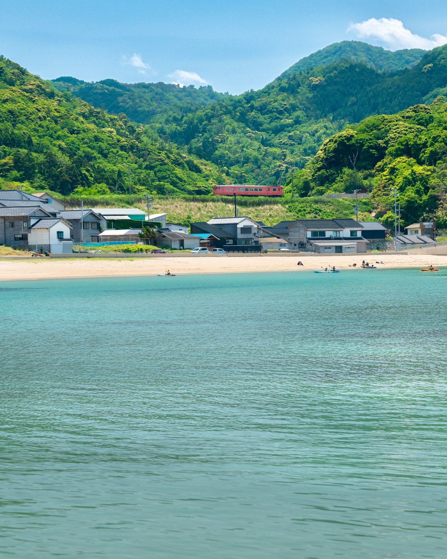 Serene beach with blue water surrounded by green mountains and small houses