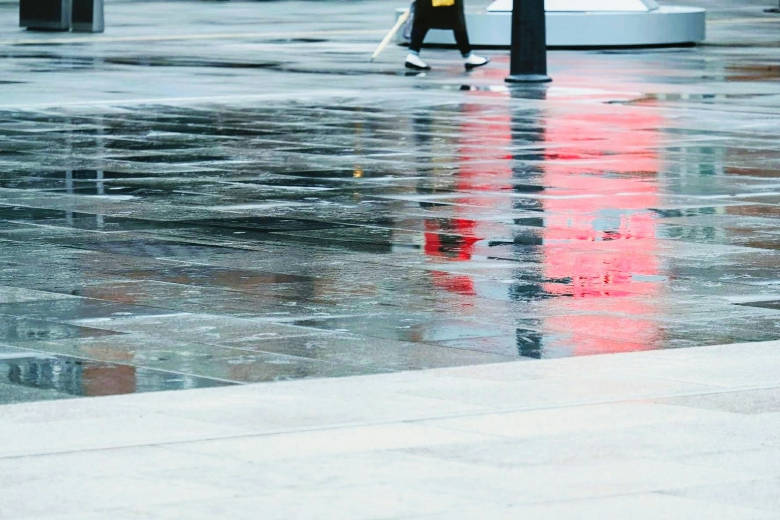 Reflection of red light on wet pavement with a person walking