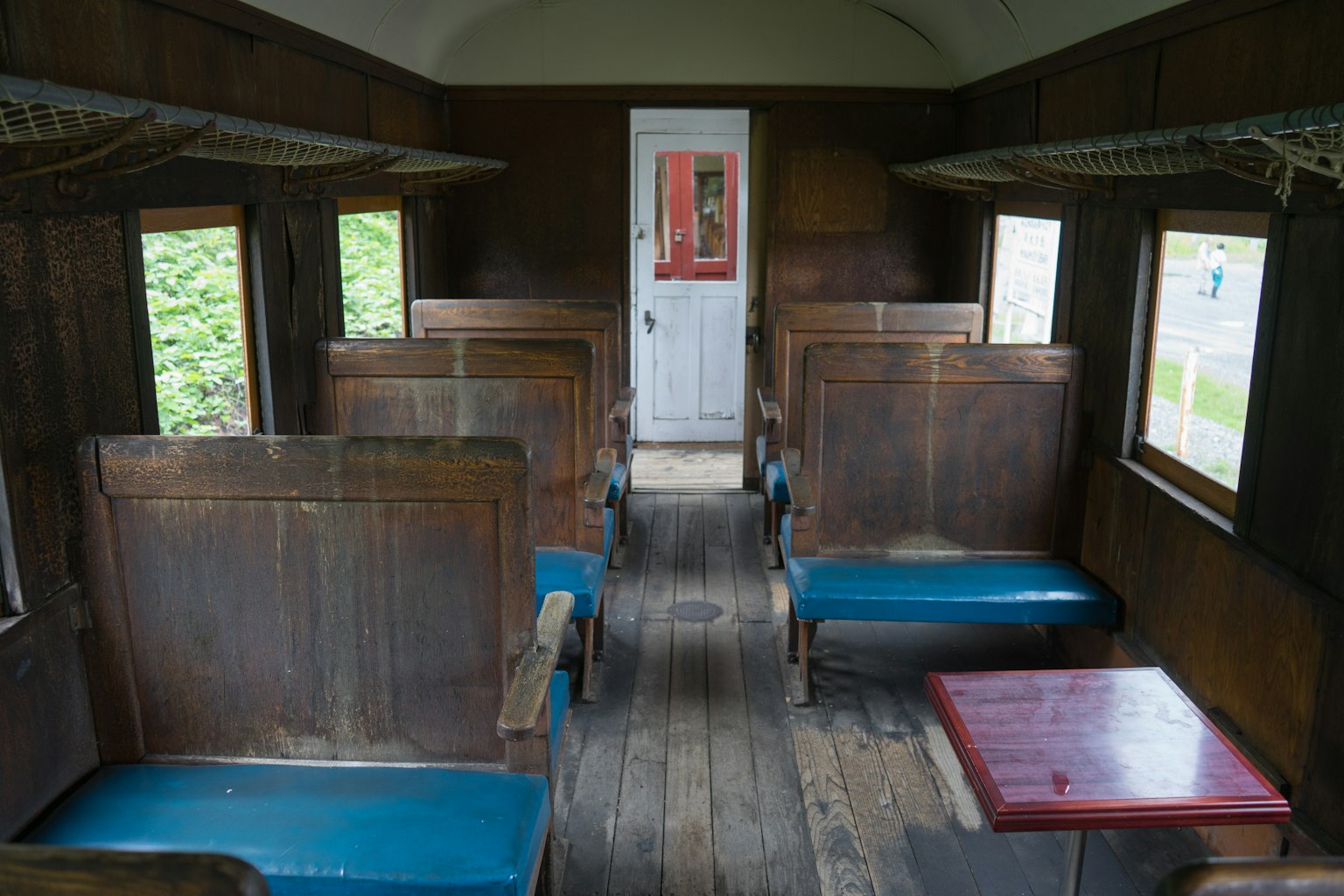 ภายในรถไฟเก่ามีผนังไม้ที่นั่งสีน้ำเงินโต๊ะกลางประตูสีแดงที่ด้านหลัง