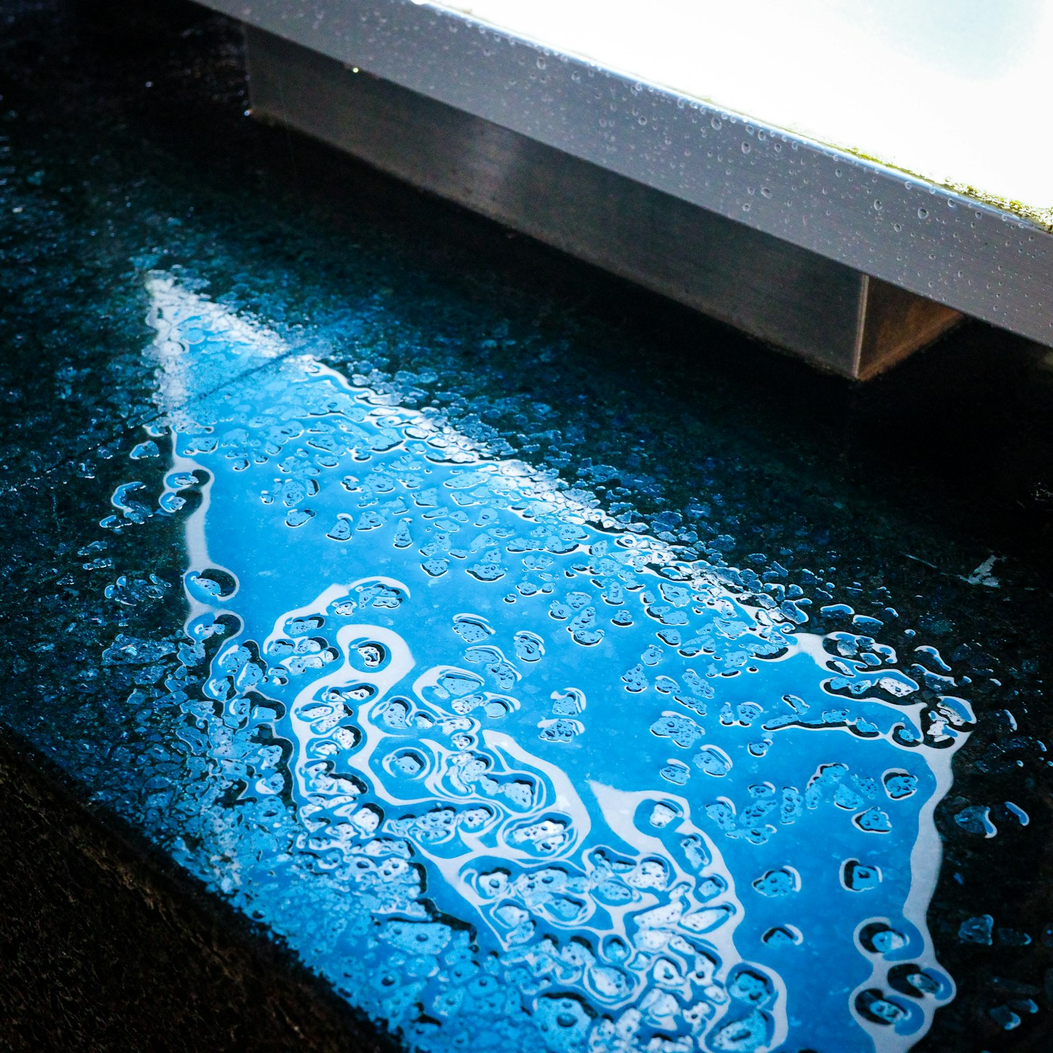 Reflection of blue light and bubble patterns on a puddle