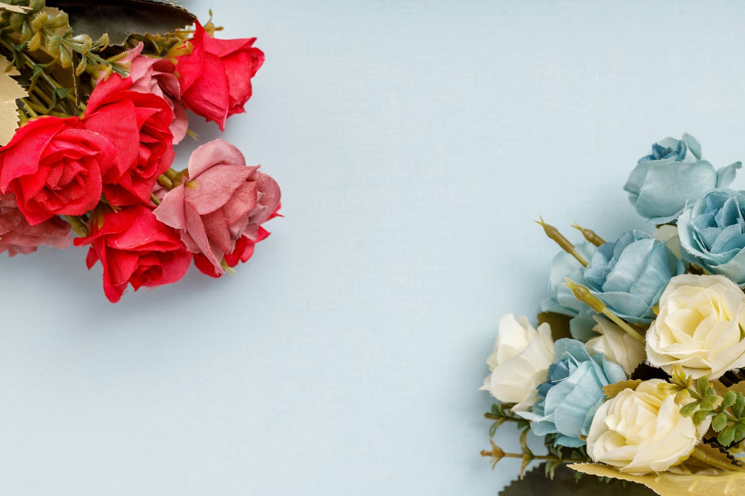 Composizione di rose rosse e pink accanto a fiori blu e bianchi su uno sfondo blu chiaro