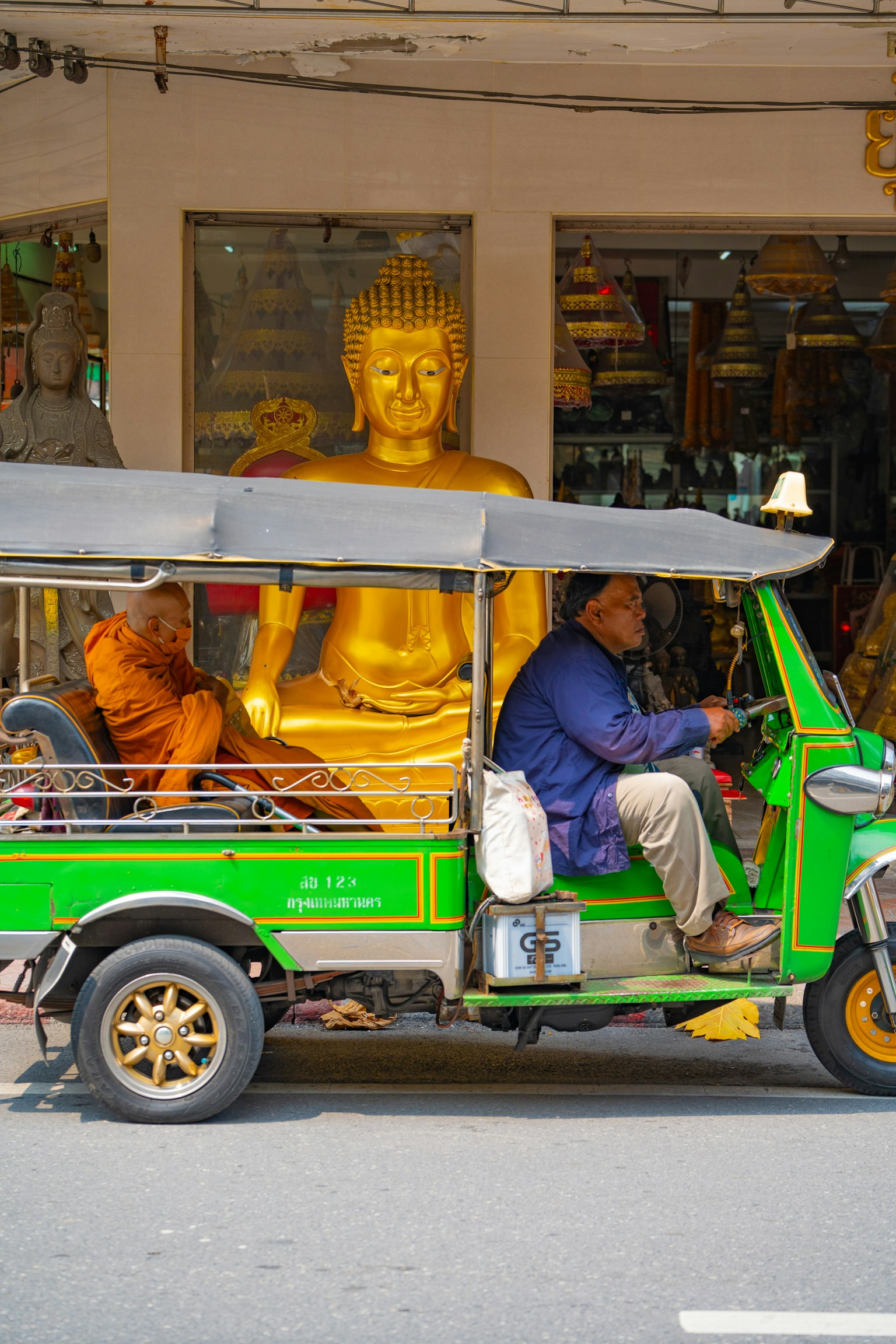 Un tuk-tuk verde pasando junto a una estatua de Buda dorada