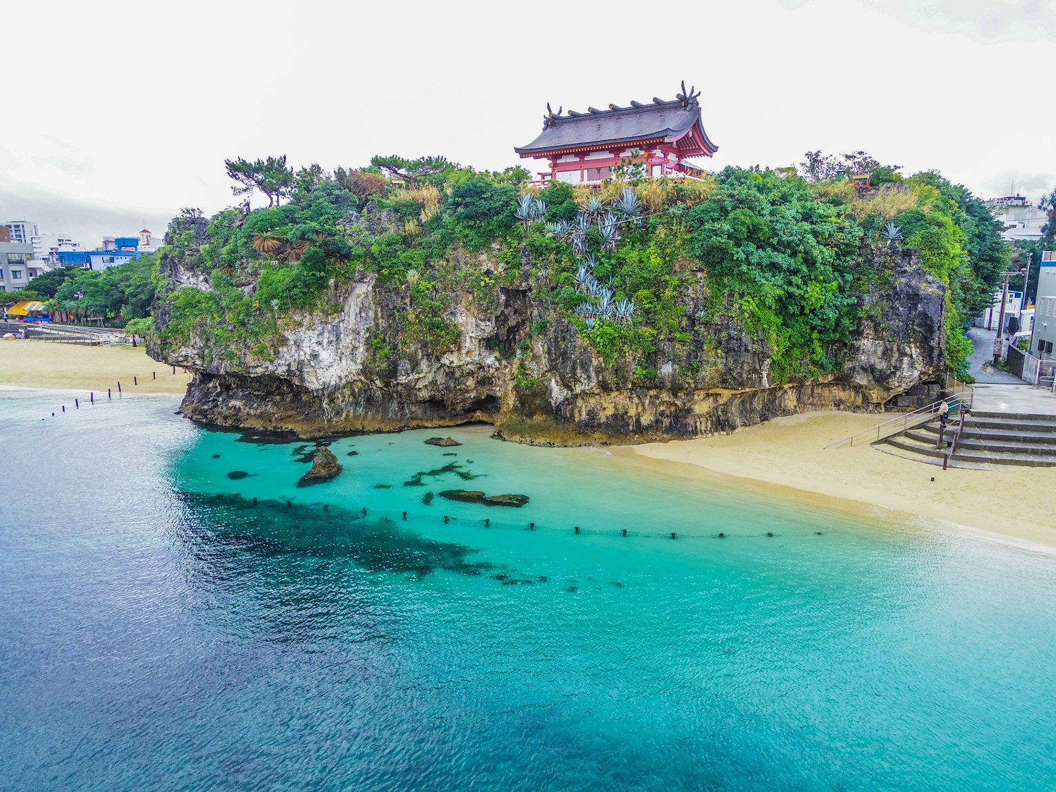 红色神社坐落在岩石上，周围是碧蓝的海水和沙滩