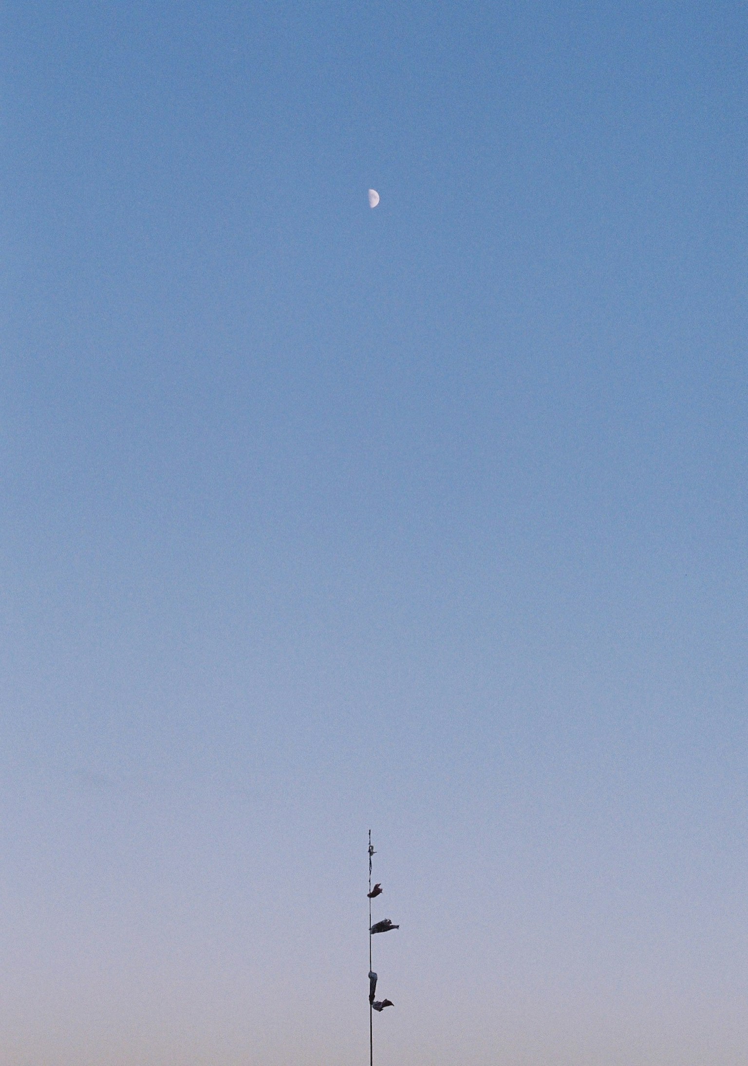 Silueta de una torre alta contra un cielo azul con una luna creciente