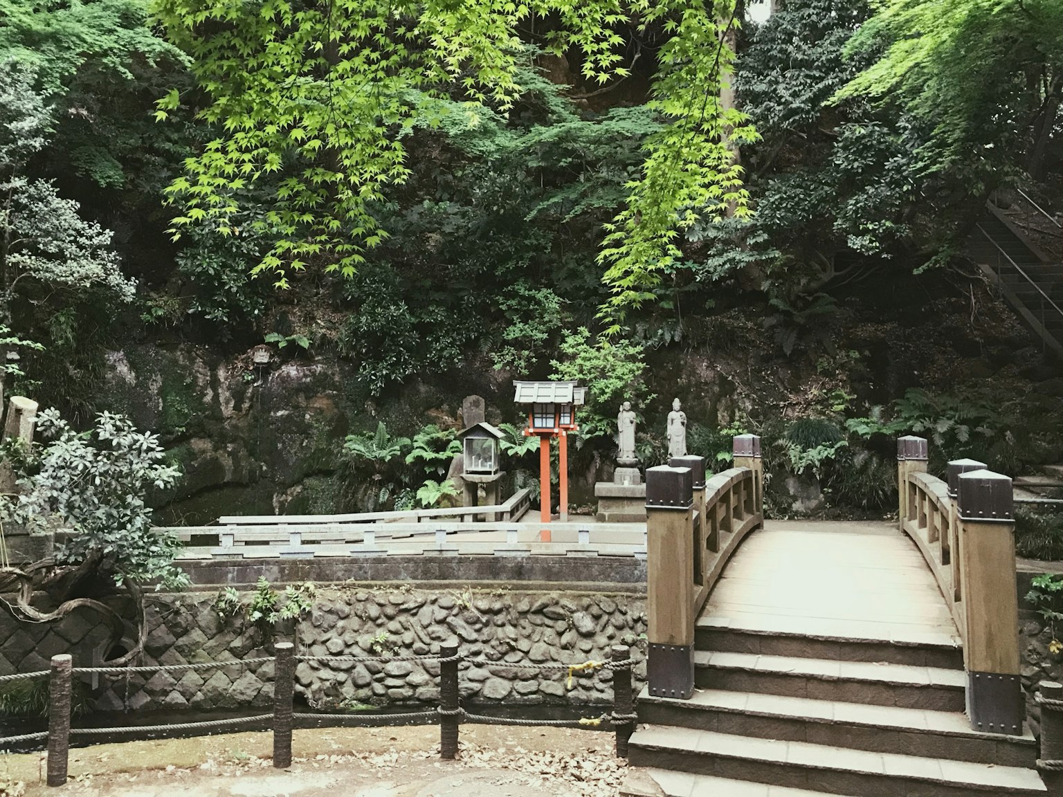 一幅寧靜的場景，木橋和石像被郁郁蔥蔥的綠色植物環繞