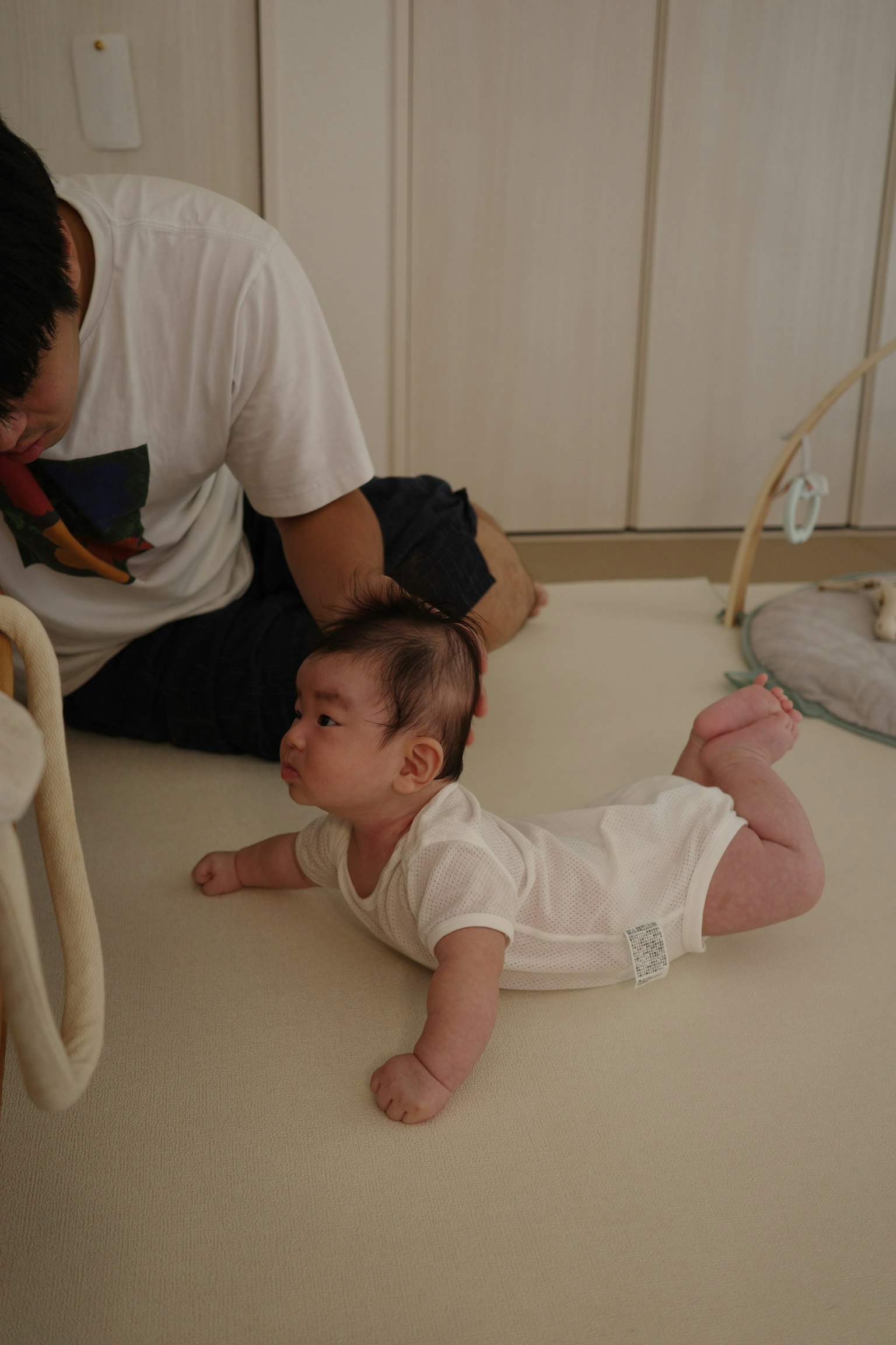 赤ちゃんが白い服を着て床にうつ伏せになっている父親の近くで遊んでいる