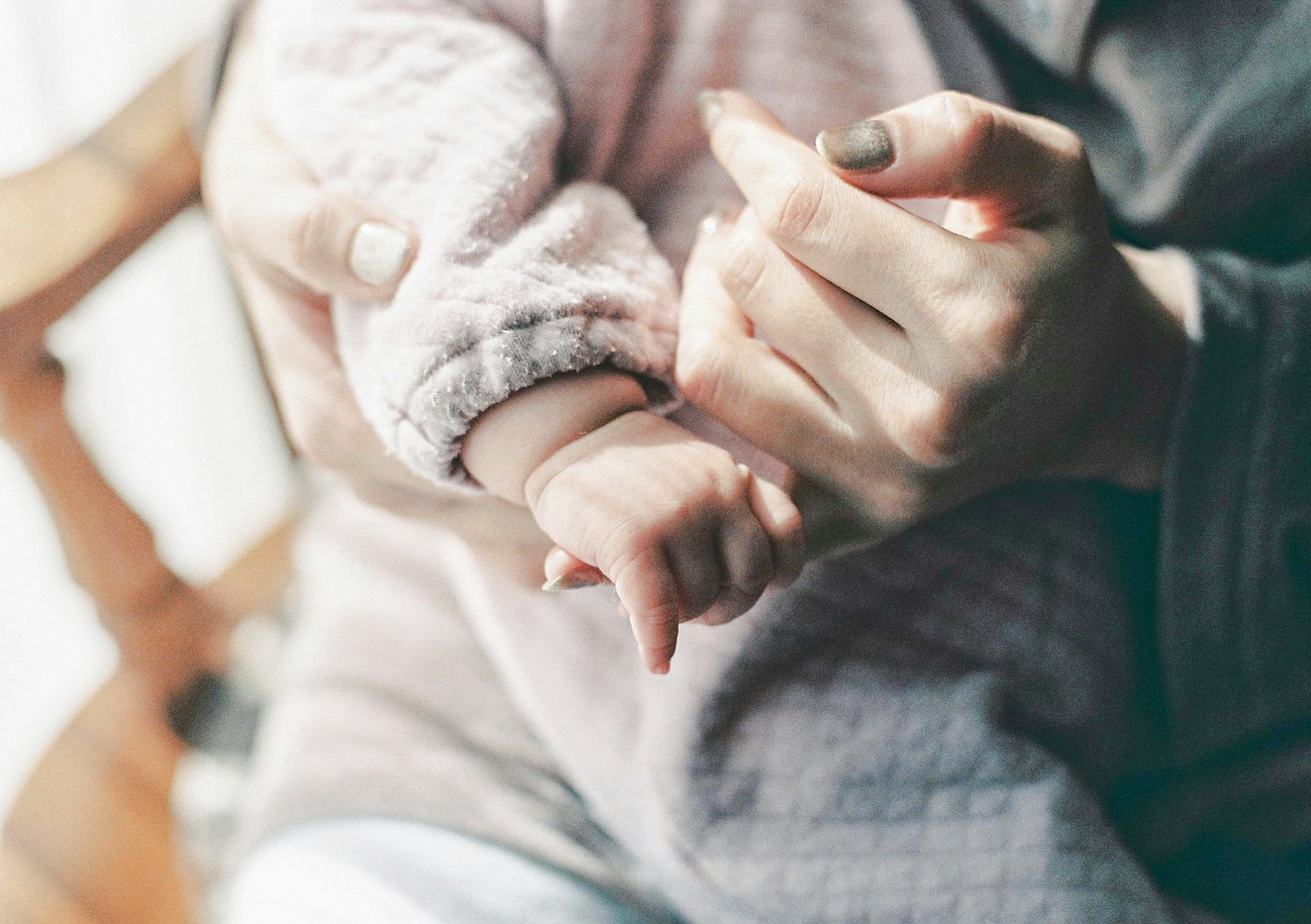Ein sanft gefärbtes Bild einer Babyhand und einer Erwachsenenhand, die sich berühren