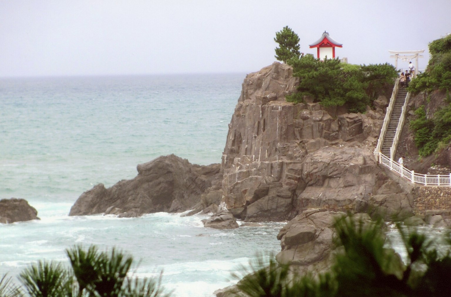 Pavillon à toit rouge sur une falaise rocheuse surplombant la mer avec une cascade