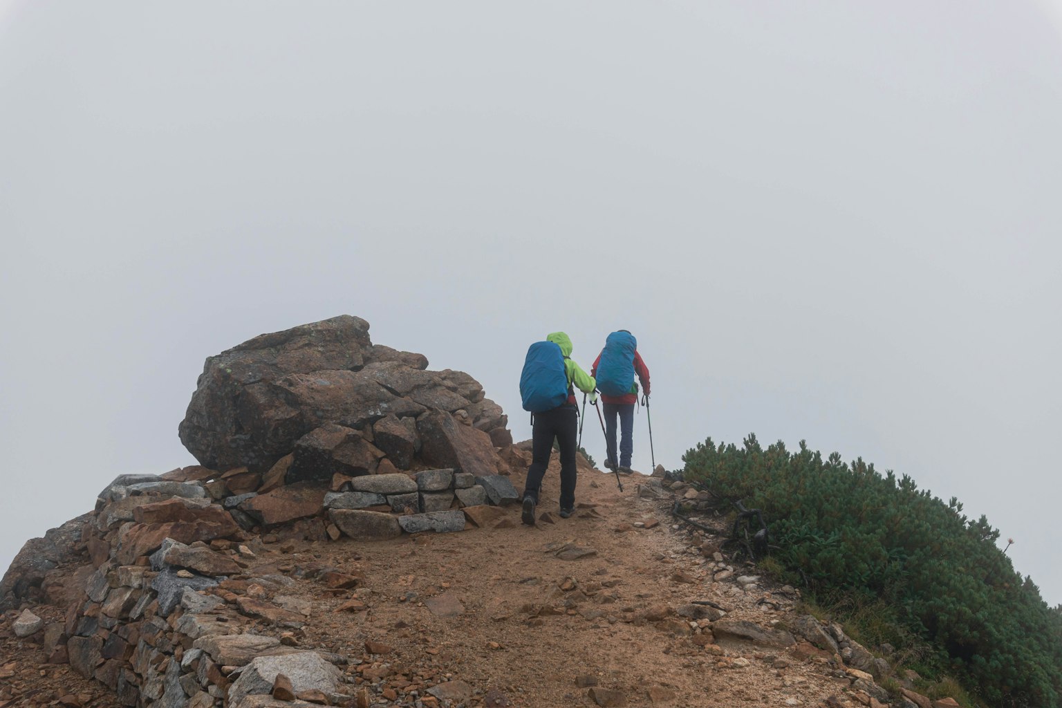 Two hikers walking on a rocky path in the fog