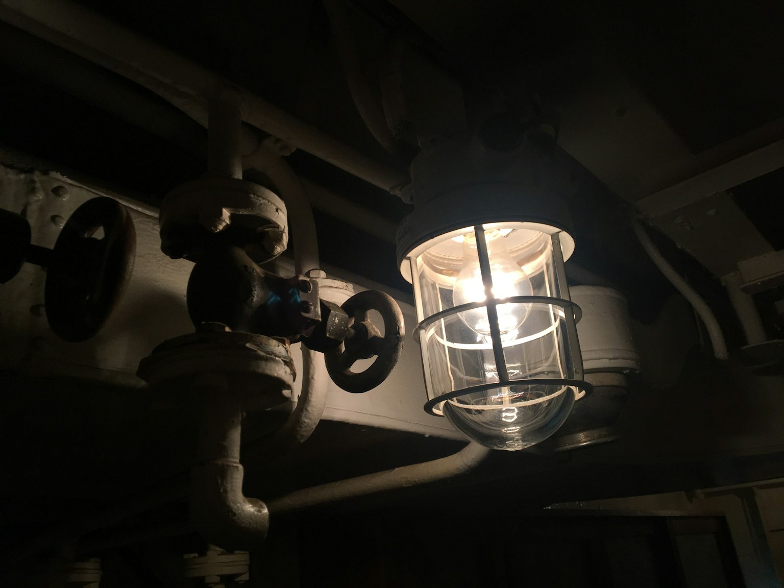 Une lampe illuminant un espace sombre avec une structure de tuyaux visible