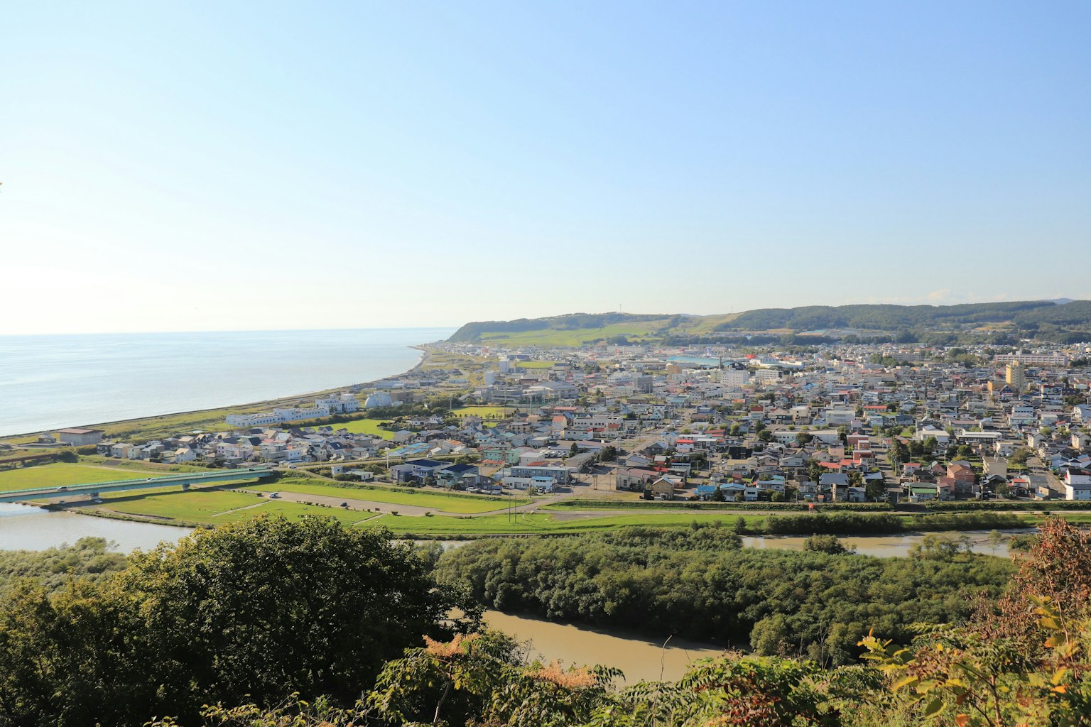 Vue panoramique d'une ville côtière avec ciel bleu et champs verts