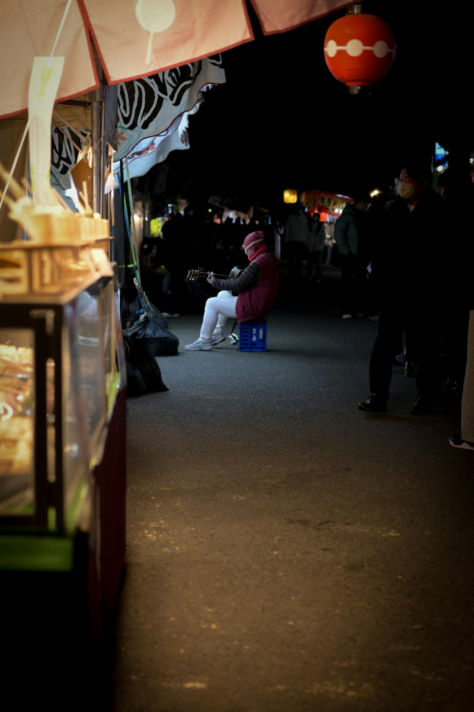 Des gens assis dans une rue bordée de stands de nourriture la nuit
