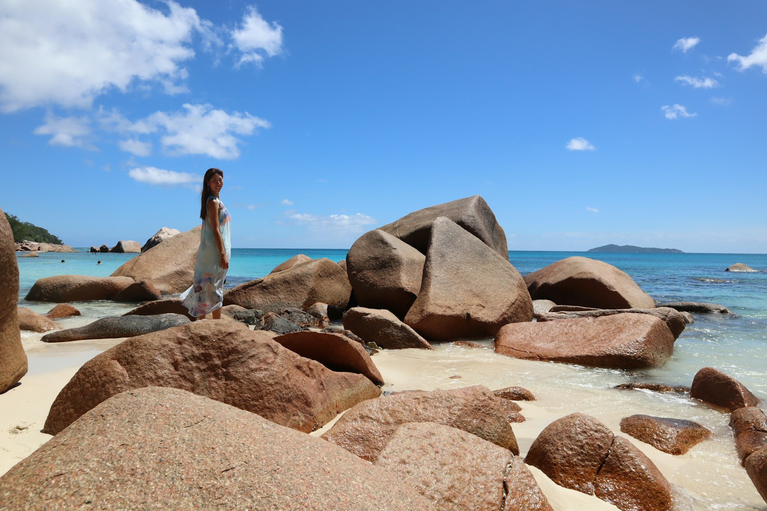 Una mujer de pie en una playa rodeada de grandes rocas y agua clara