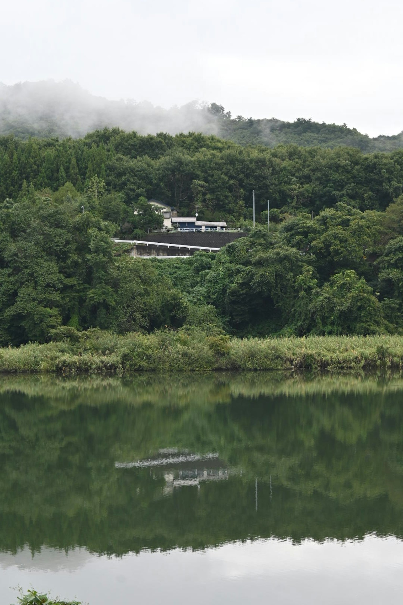 Un edificio situato su colline verdi accanto a un lago tranquillo che riflette il paesaggio