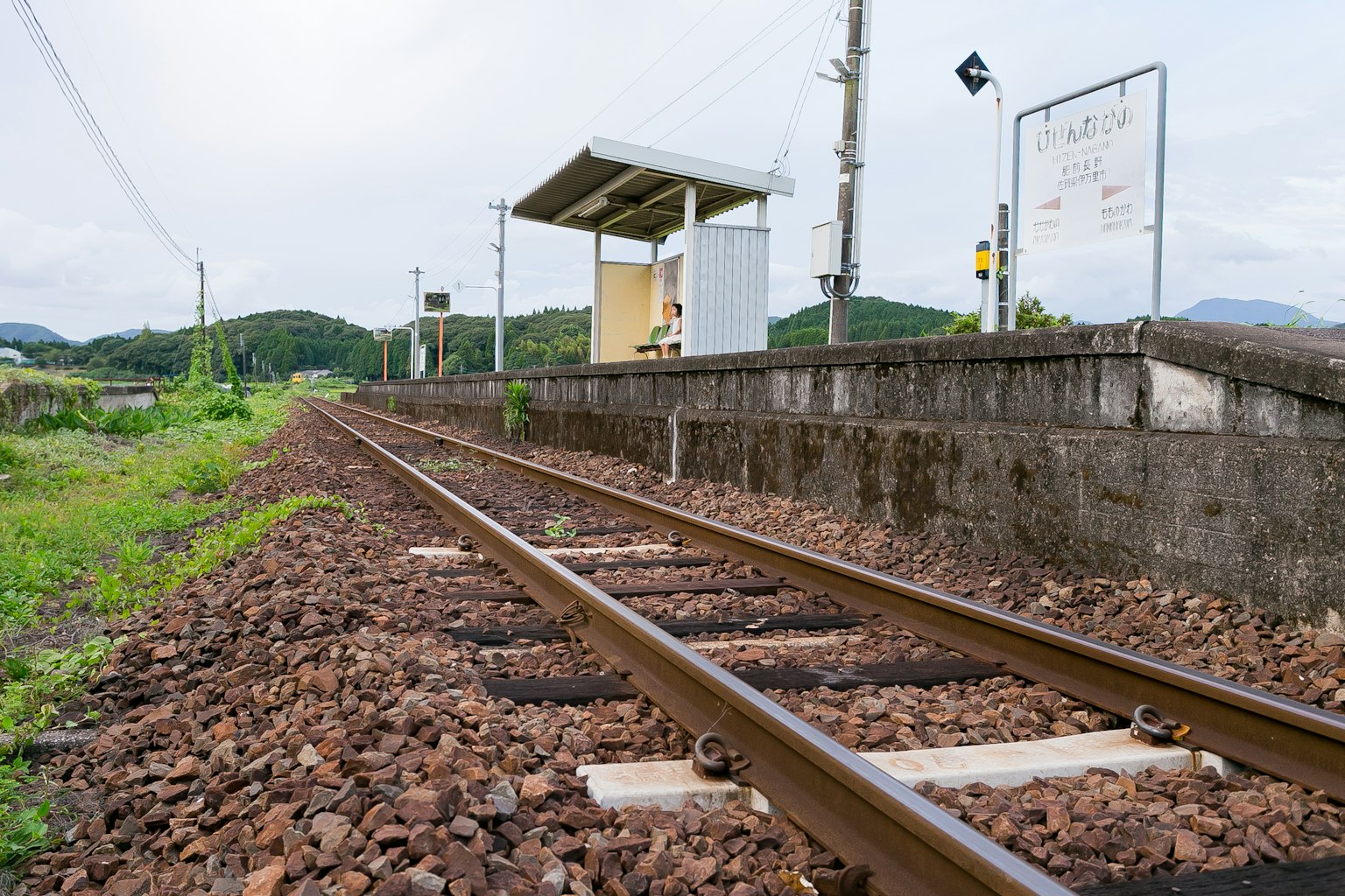 Rails de chemin de fer avec une petite gare entourée de verdure et de collines