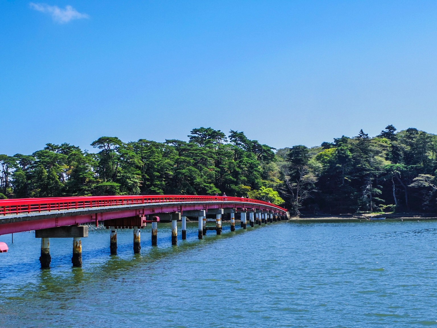 Un puente rojo se extiende sobre el agua bajo un cielo azul claro