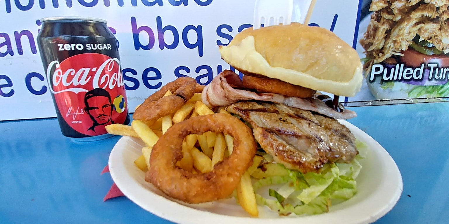 Ein Teller mit einem Hamburger, Pommes Frites, Zwiebelringen und einer Dose Coca-Cola