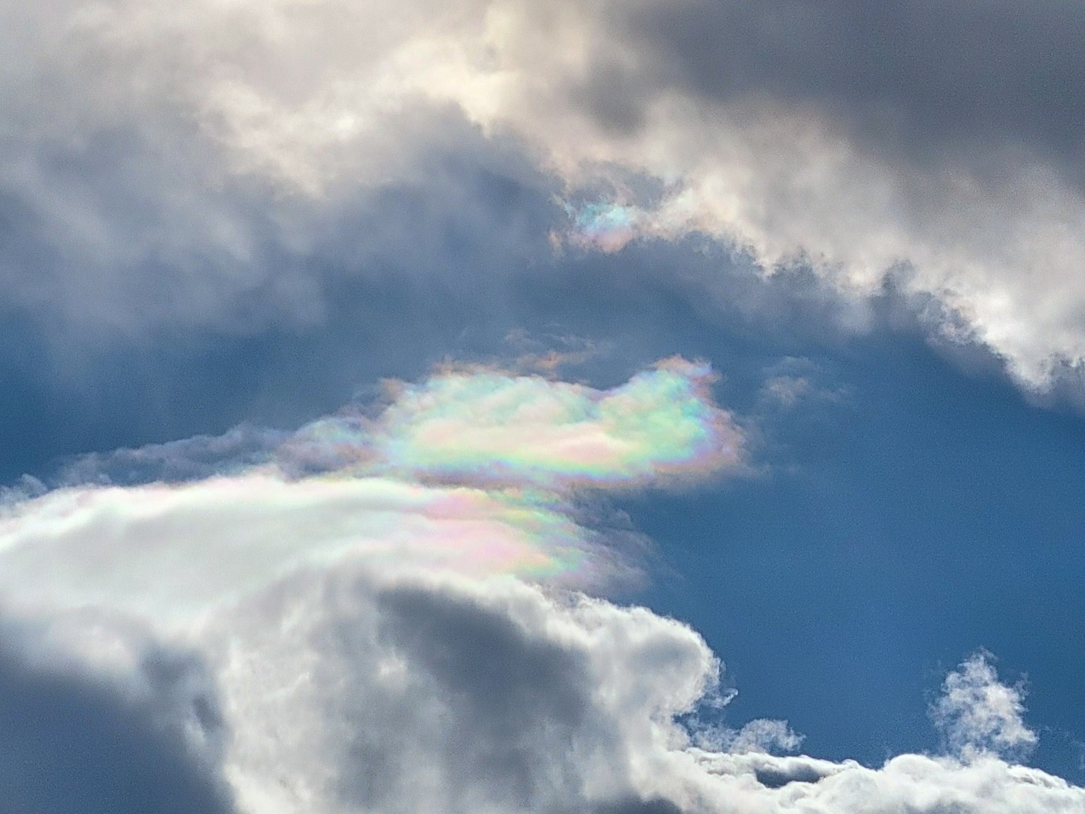 Iridescent cloud formation against a blue sky with white clouds