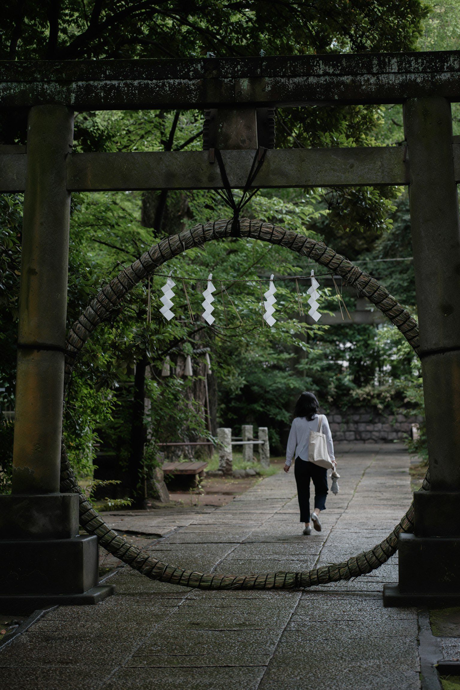 Eine Frau in Weiß, die durch ein Torii geht, umgeben von üppigen grünen Bäumen