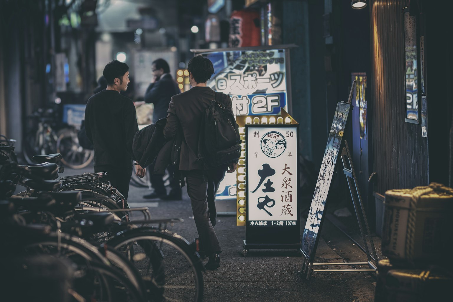 Due uomini che camminano in una strada notturna con insegne di ristorante