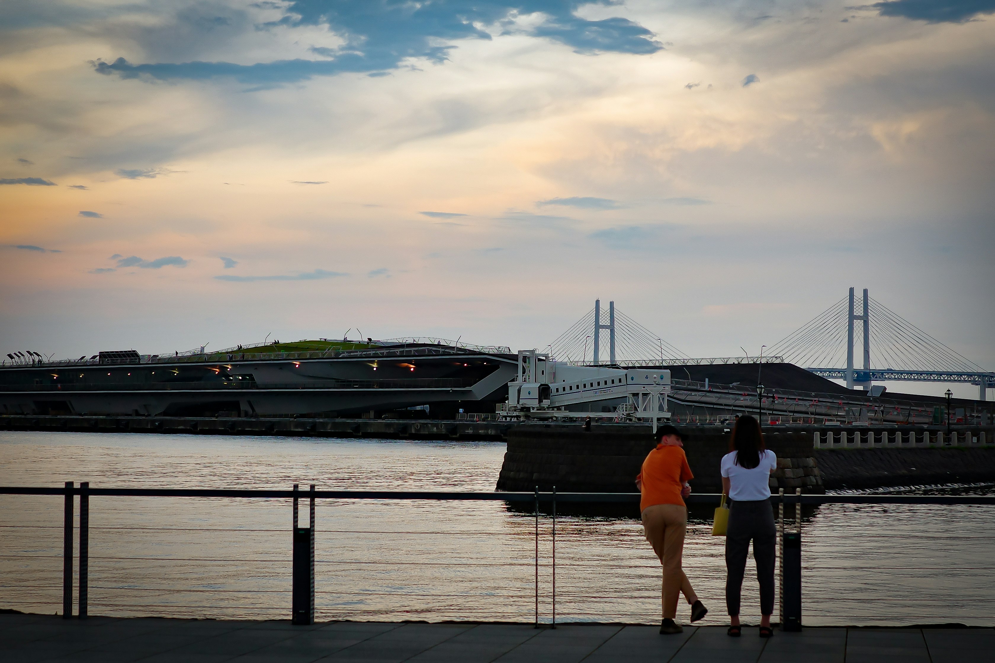People walking along a riverside promenade with a docked ship
