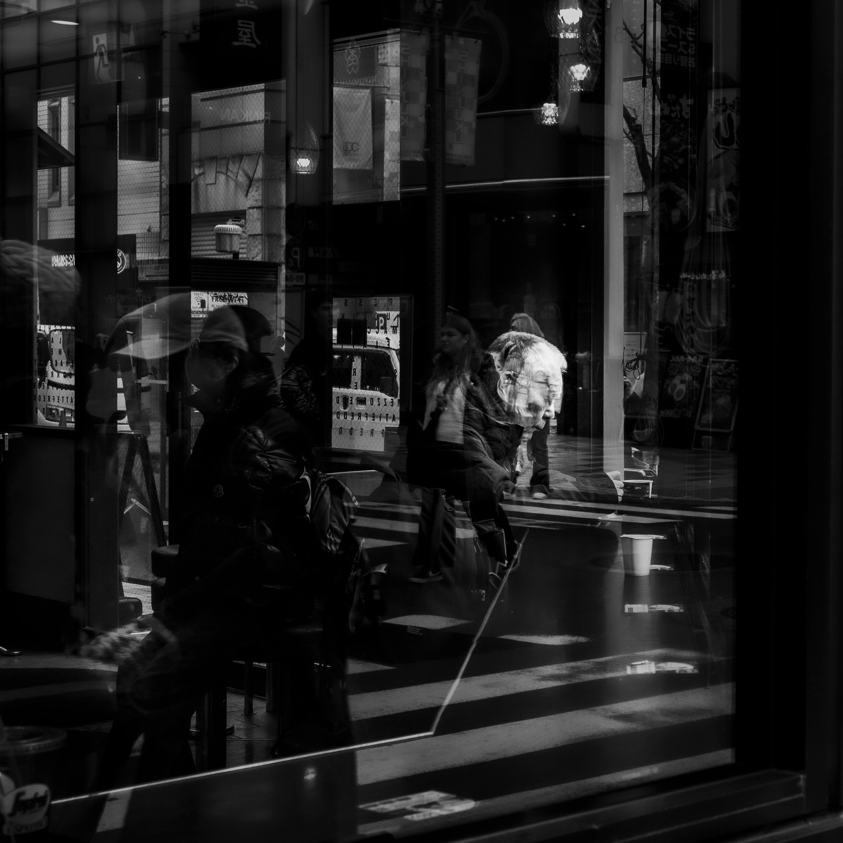 夜の街角でガラス越しに人が行き交う路地のスナップ