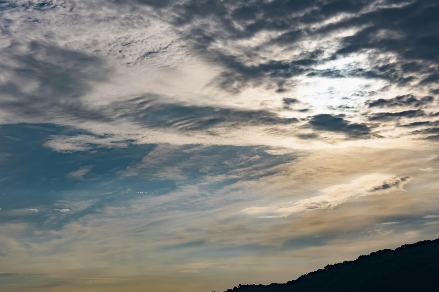 Clouds in a blue sky with a silhouette of a mountain