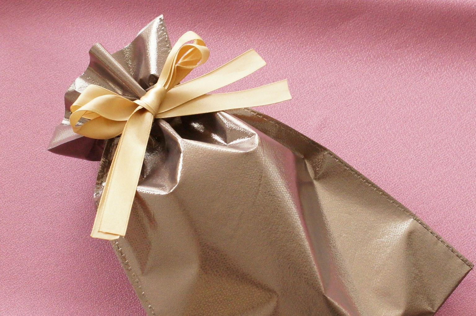Geschenk in glänzendem Goldfolie mit einer cremefarbenen Schleife verpackt