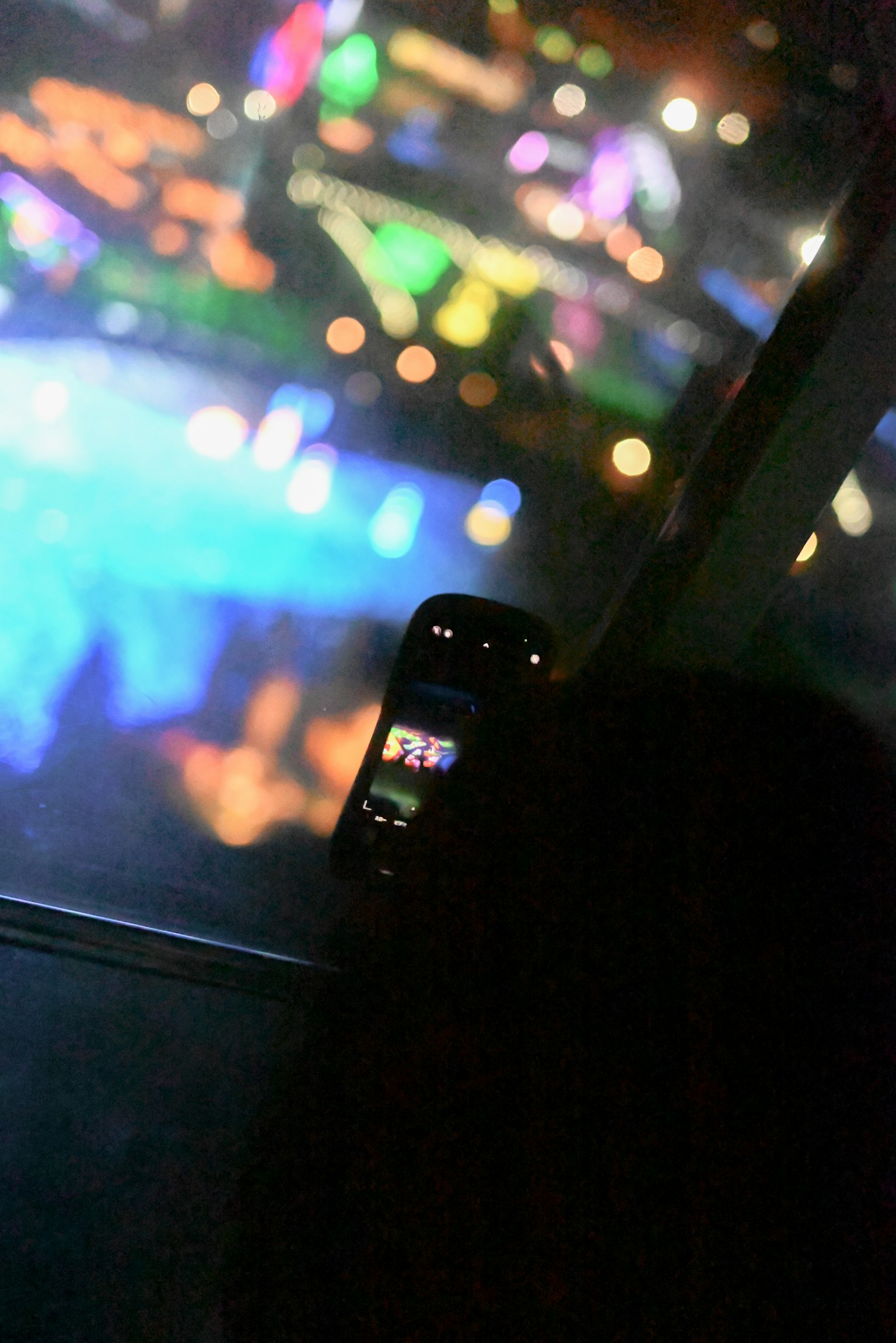 Foto einer Person in der Nähe eines Fensters, die Stadtlichter mit einem Mobiltelefon aufnimmt, bunte Reflexionen im Hintergrund