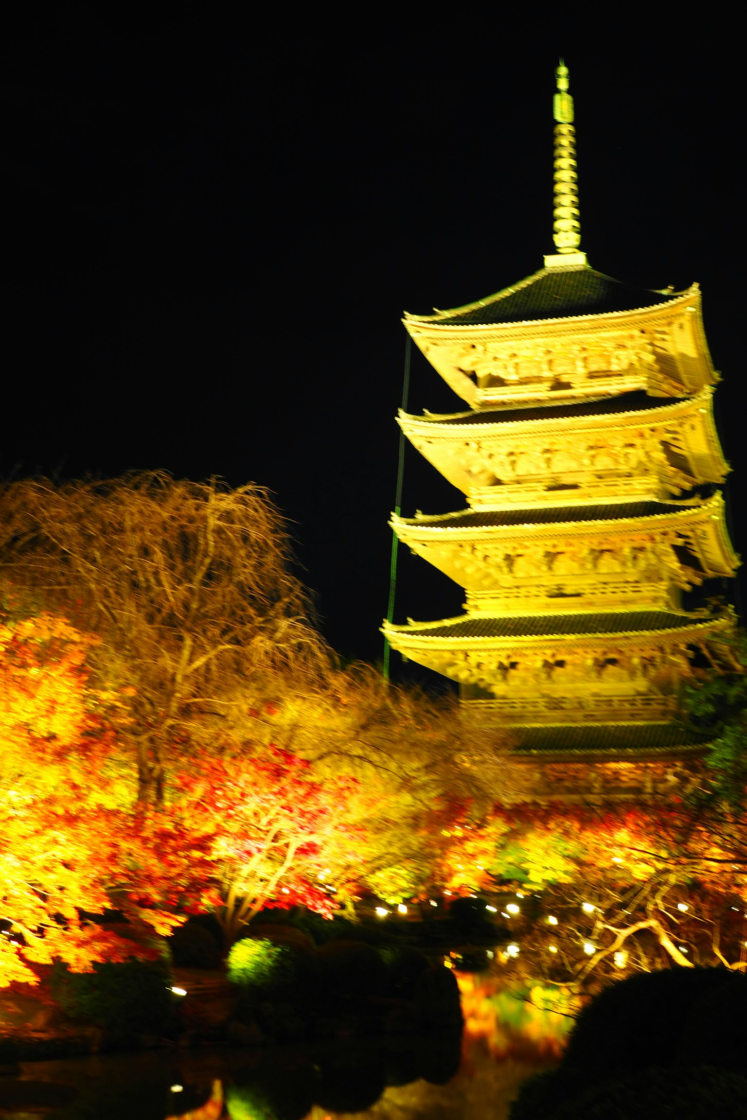 Tháp ba tầng màu vàng được chiếu sáng vào ban đêm, xung quanh là lá mùa thu nhiều màu sắc