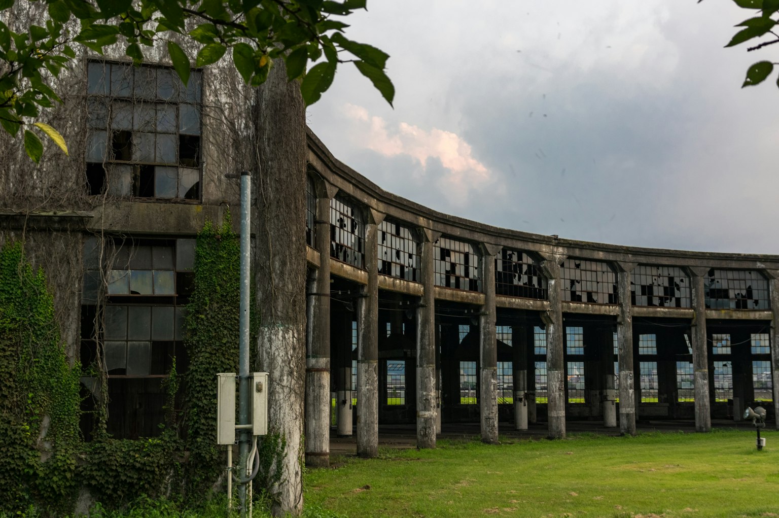 Abandoned building with large windows surrounded by overgrown grass