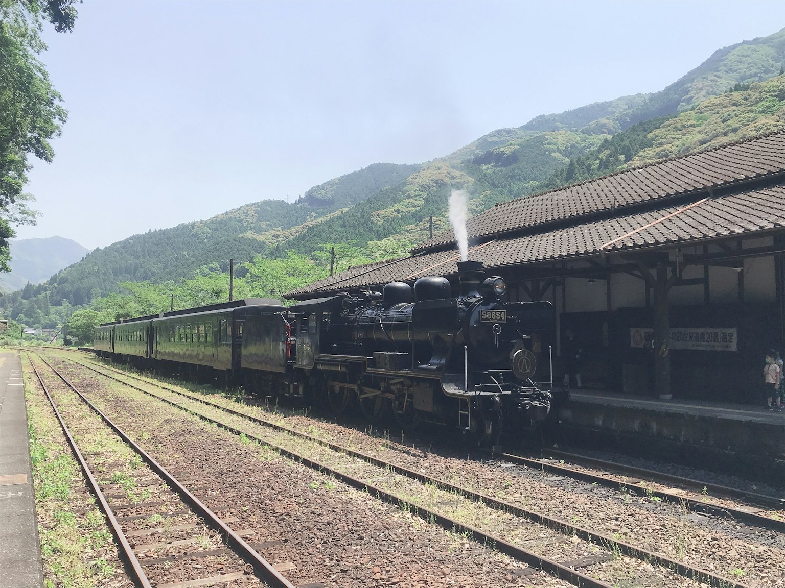 蒸汽機車在車站停靠，周圍是綠色的山脈