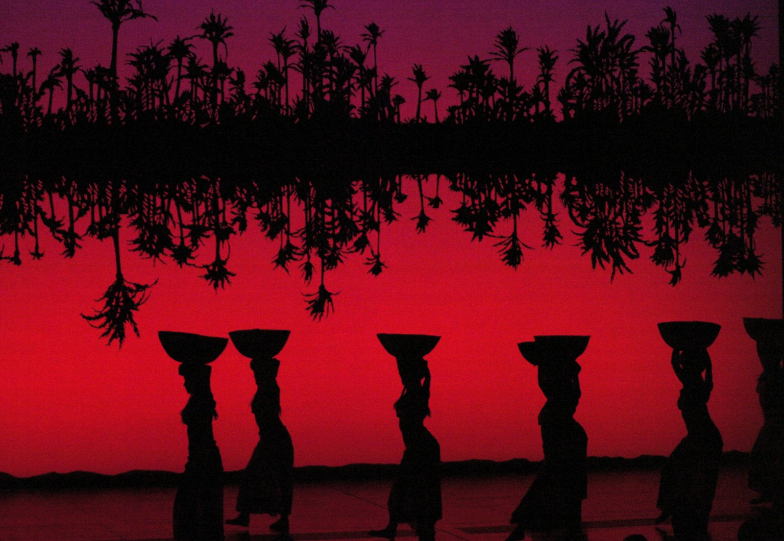 Silhouette di donne che trasportano acqua sotto un cielo rosso al tramonto