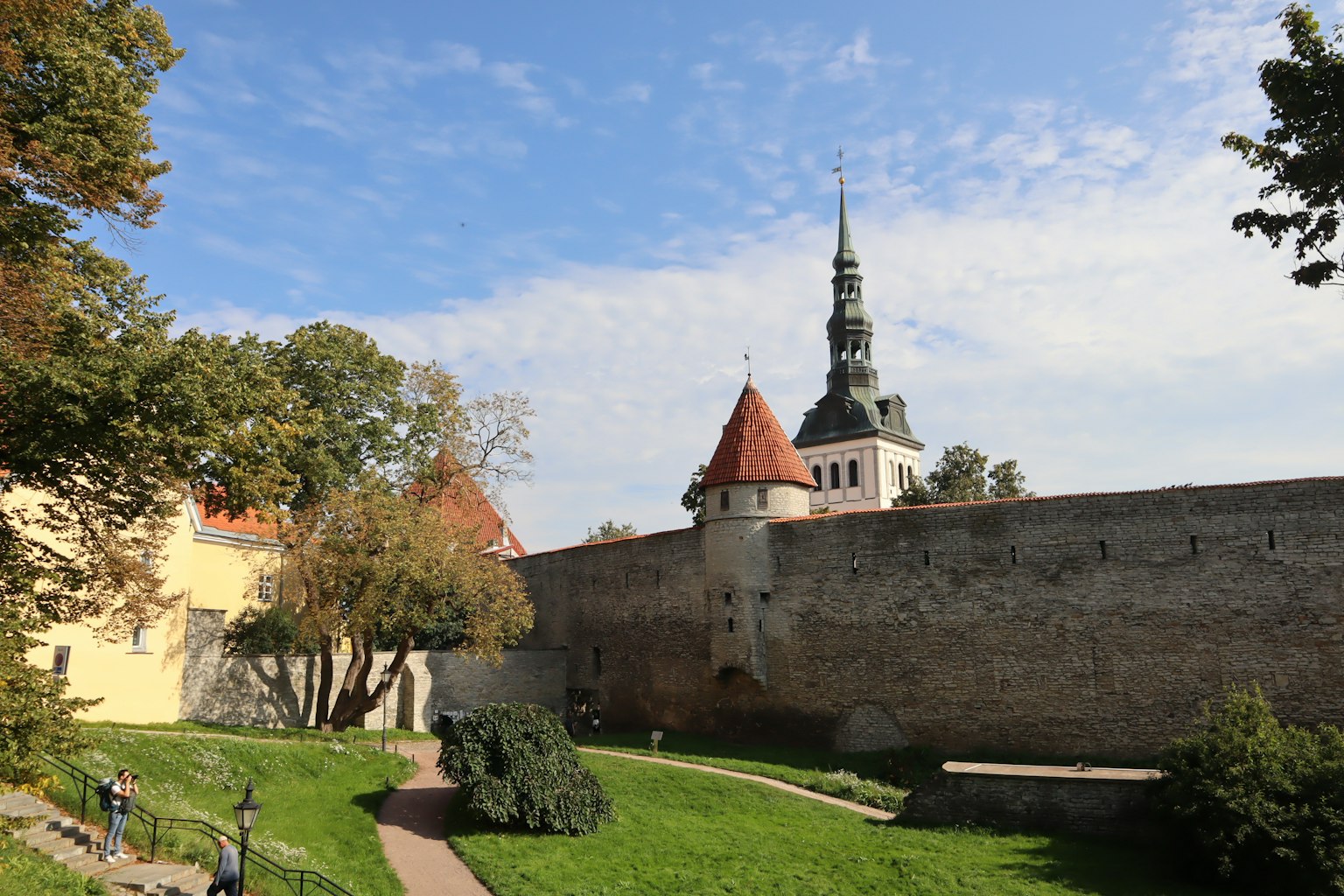 Malerscher Blick auf grünes Gras und historische Mauern mit einem Spitzenturm und roten Dächern