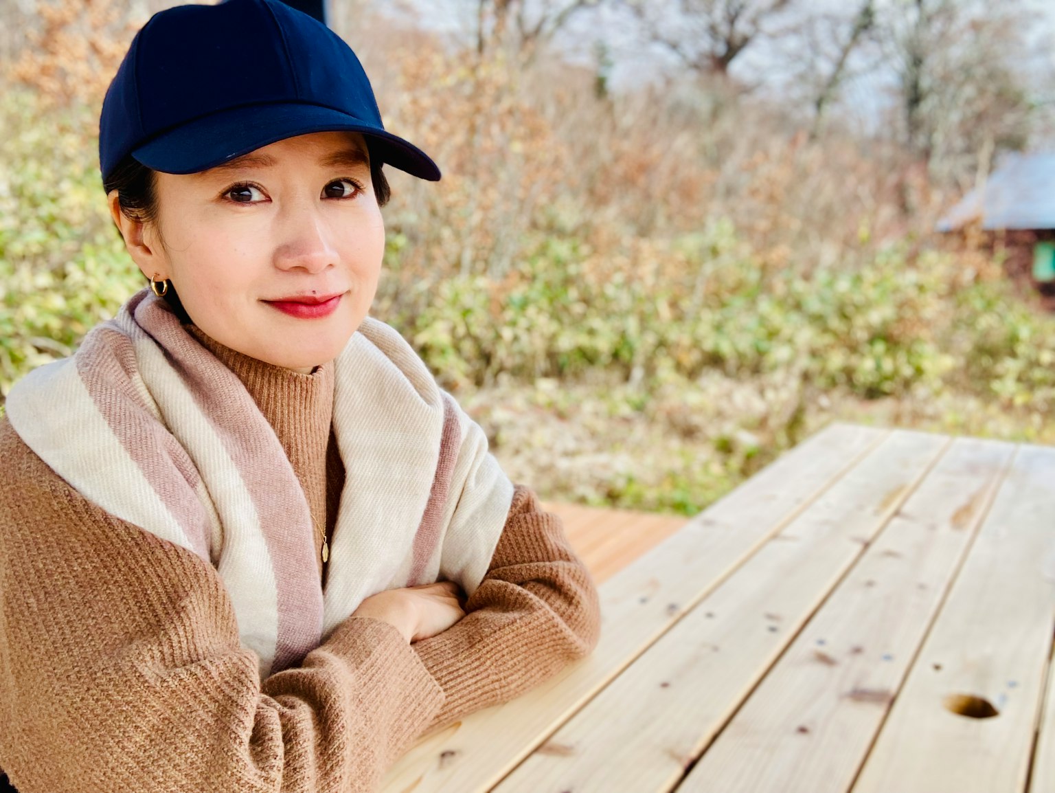 캐주얼한 복장의 여성이 나무 테이블에 앉아 있고 배경에는 자연이 펼쳐져 있다