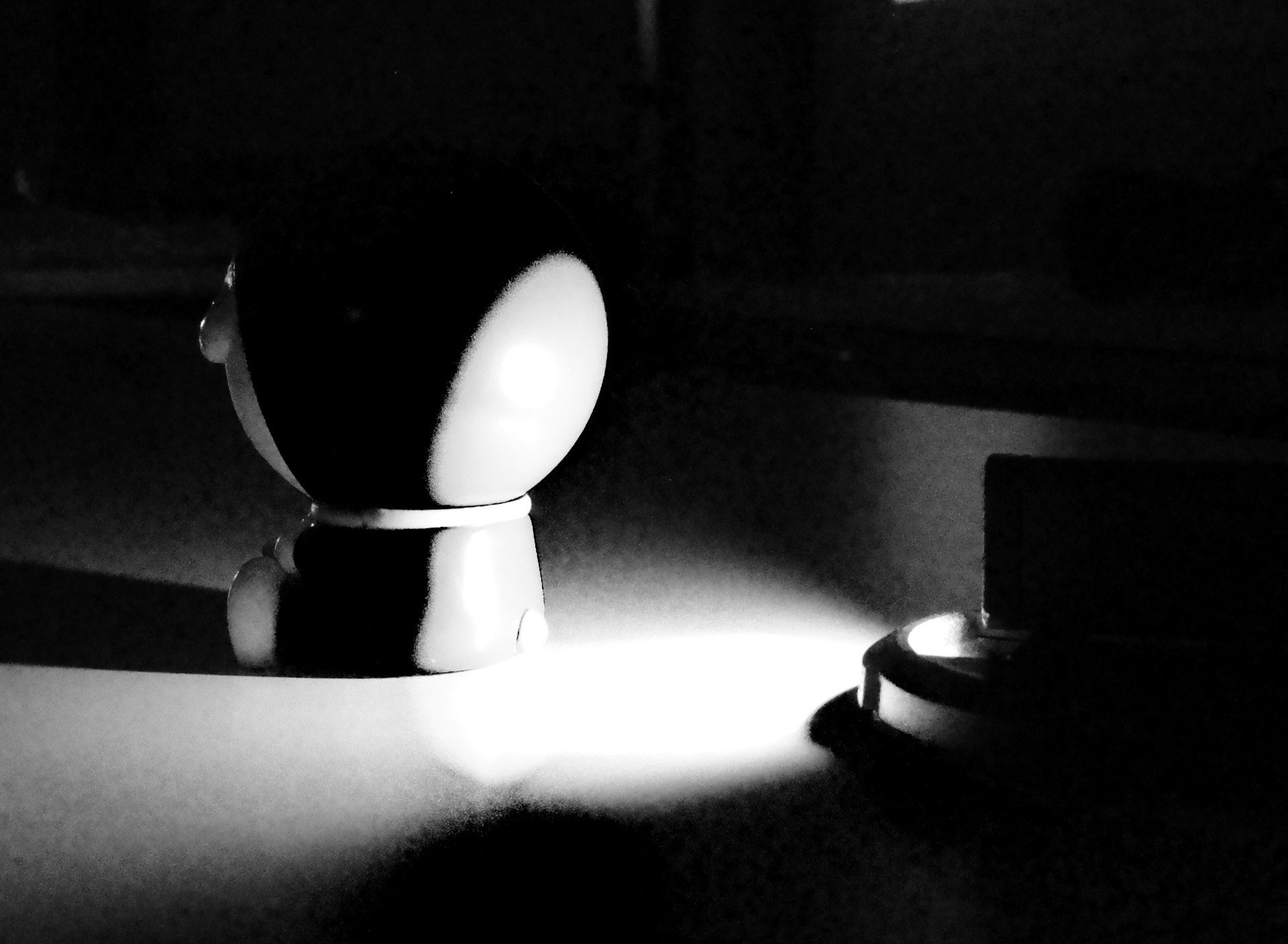 暗い背景に白い光を受けた黒いオブジェクトと小さなランプが映る画像